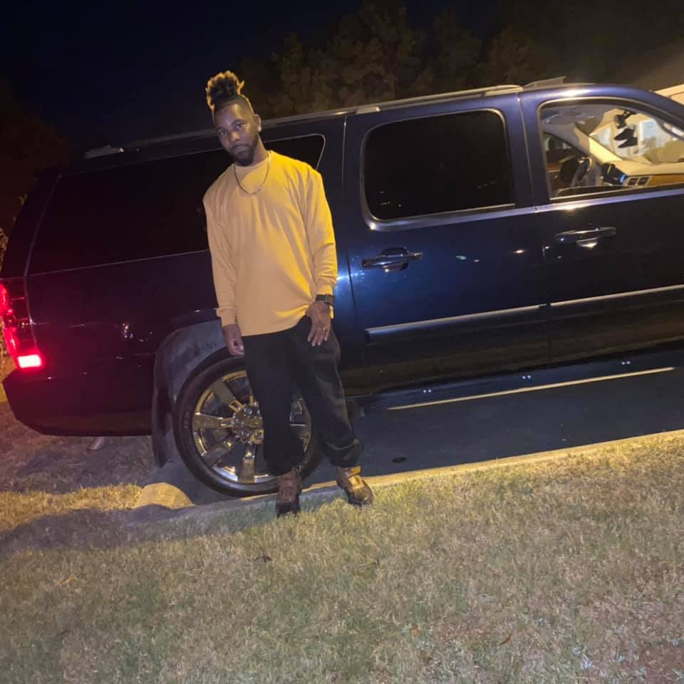 A man standing next to a black SUV at night on grass