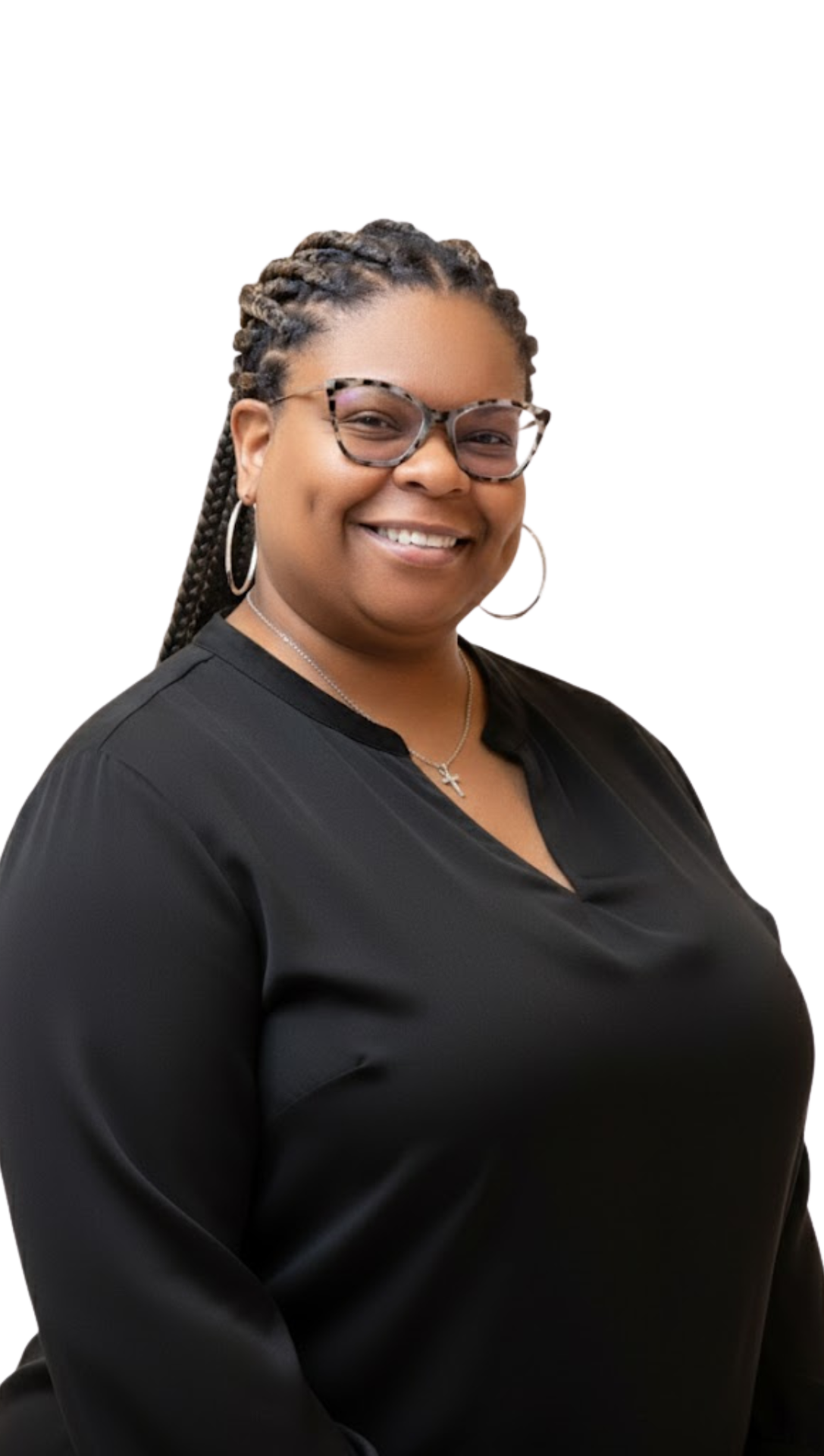 A woman with braids, glasses, and hoop earrings smiling, wearing a black top and a cross necklace against a black background.