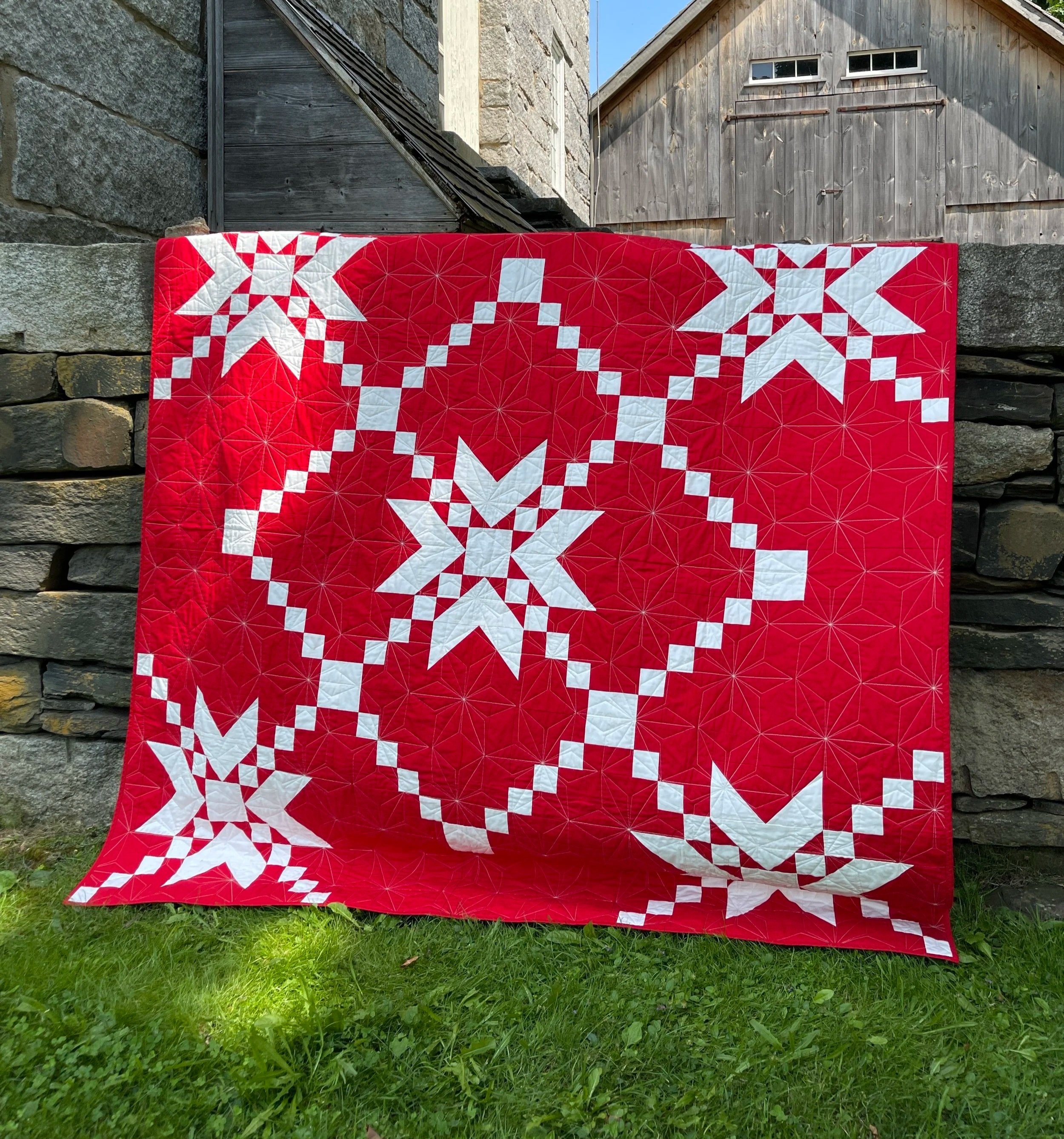 A five star Irish Chain inspired quilt hanging on a stone wall.