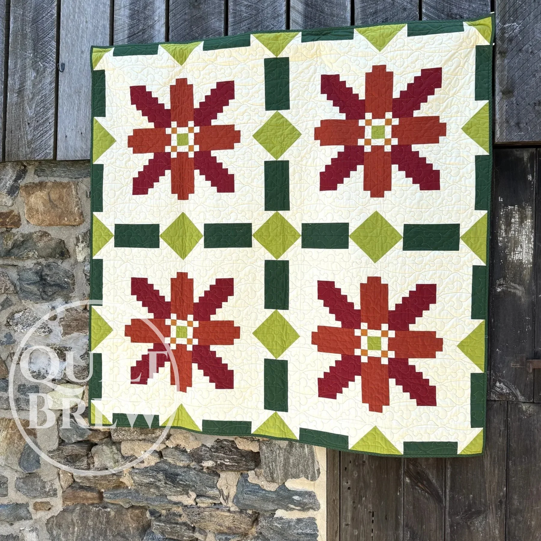 A quilt that looks like poinsettias is hanging on an old stone barn.