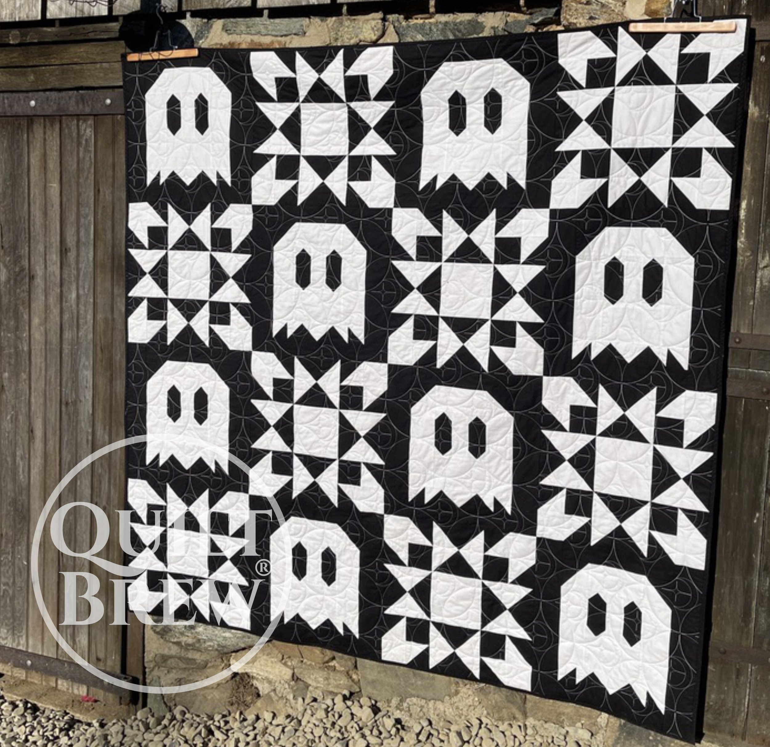 A quilt with ghost and star blocks hangs on a barn door.