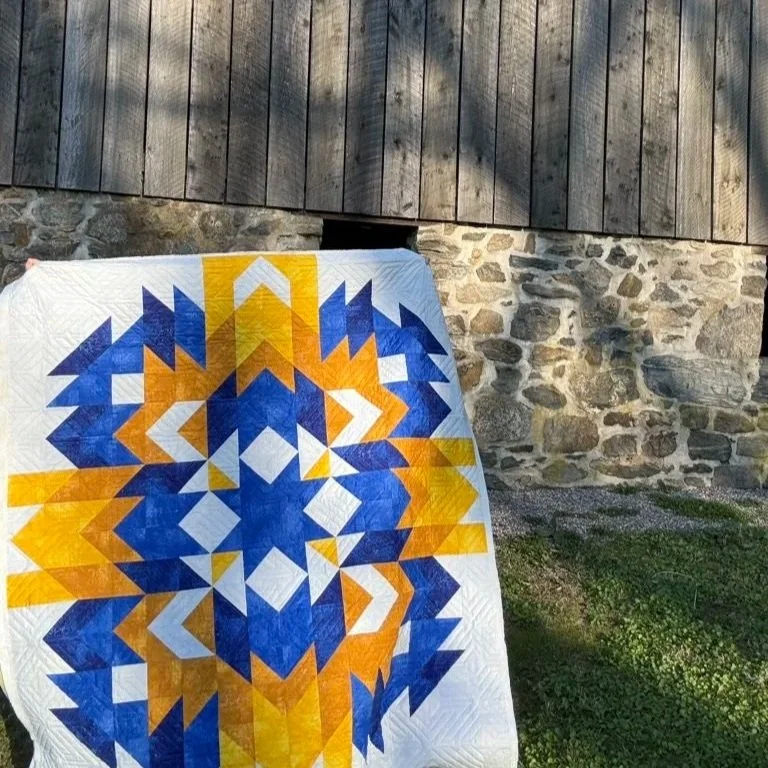 A person is holding up a quilt that has triangular shapes bursting from the center.