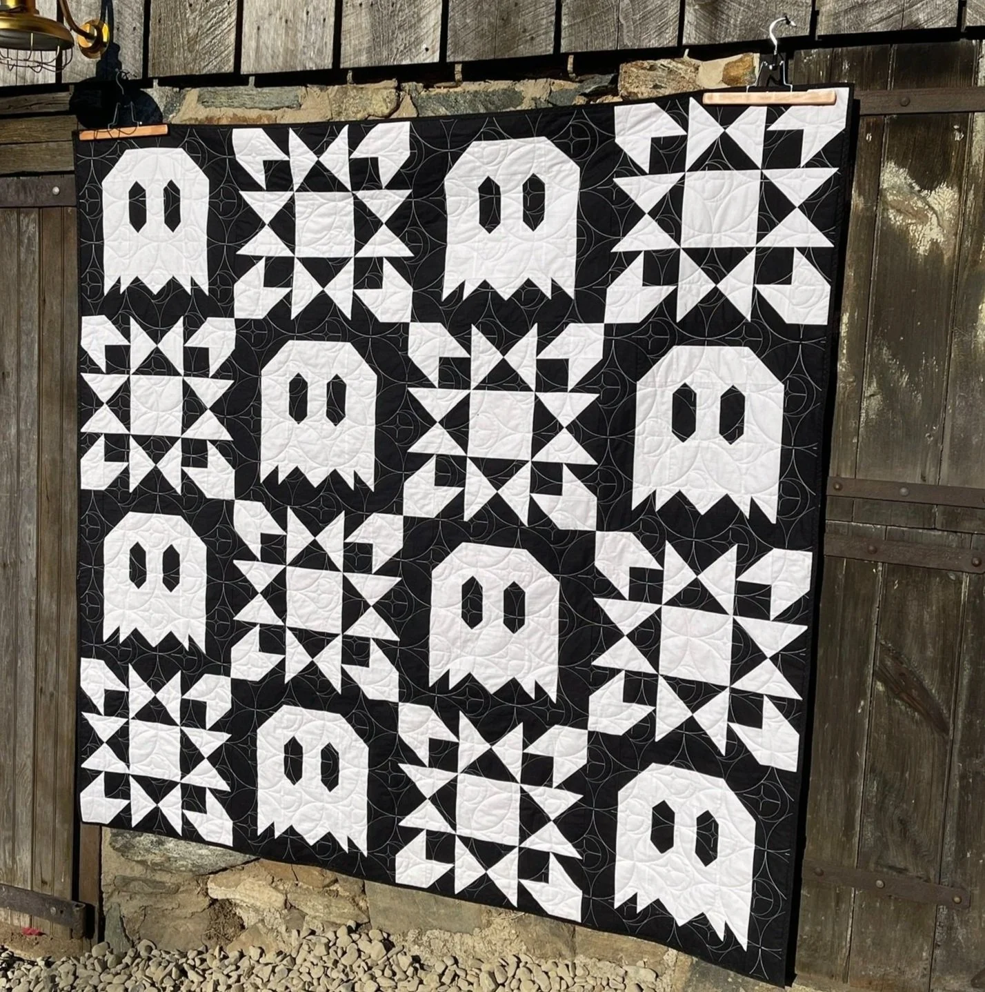 A quilt with ghost and star blocks hangs on a barn door.