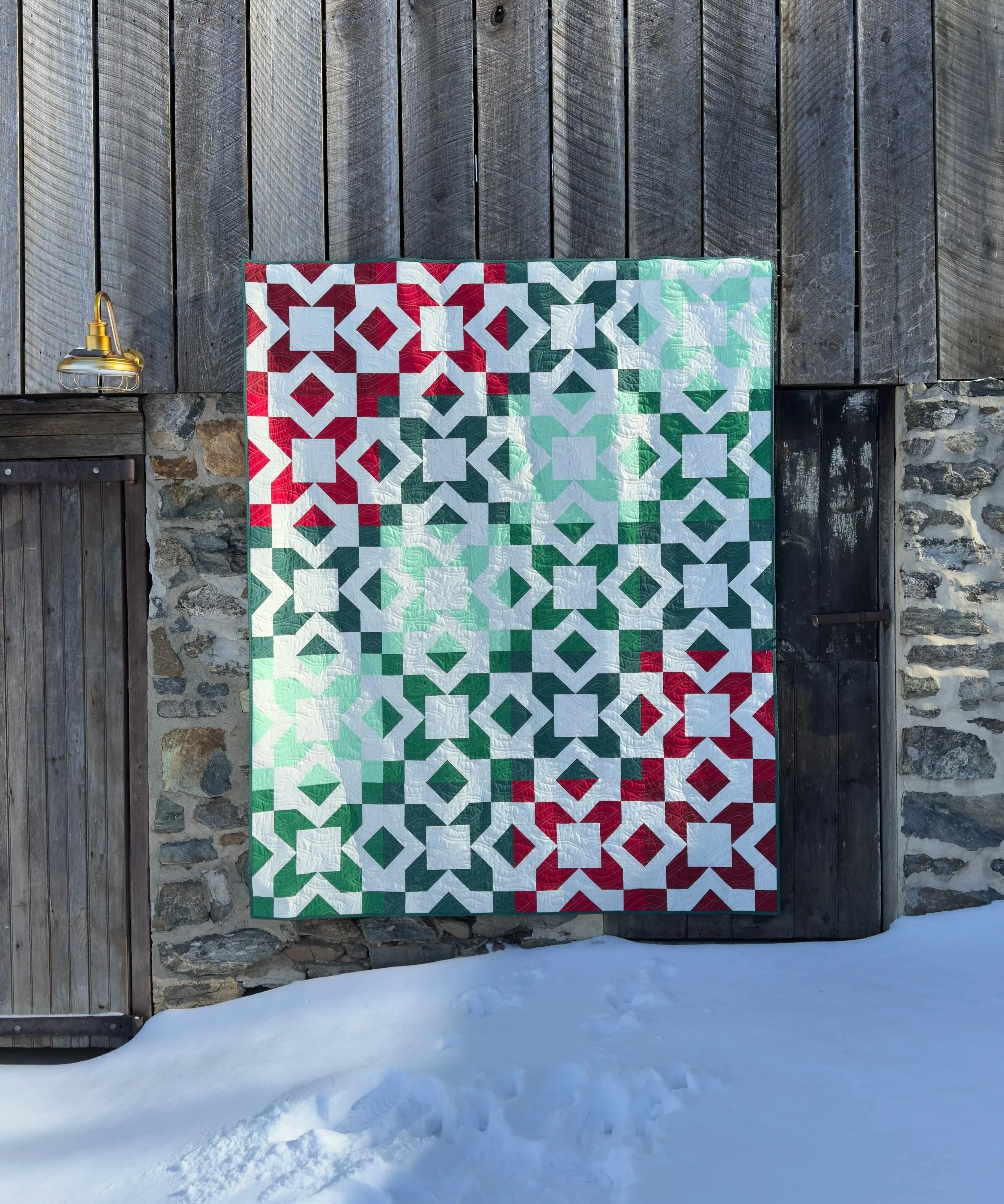 Image of a someone holding a quilt made of star blocks in front of a large stone barn.