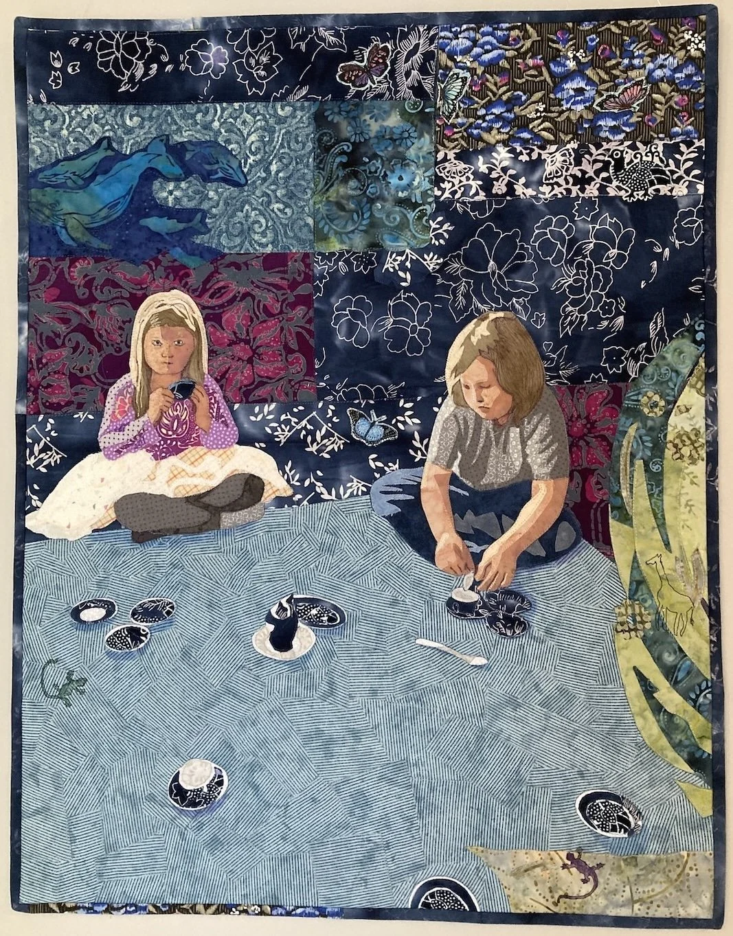 Two children sit on the floor and drink tea from a miniature tea set. Plants and animals  surround them.