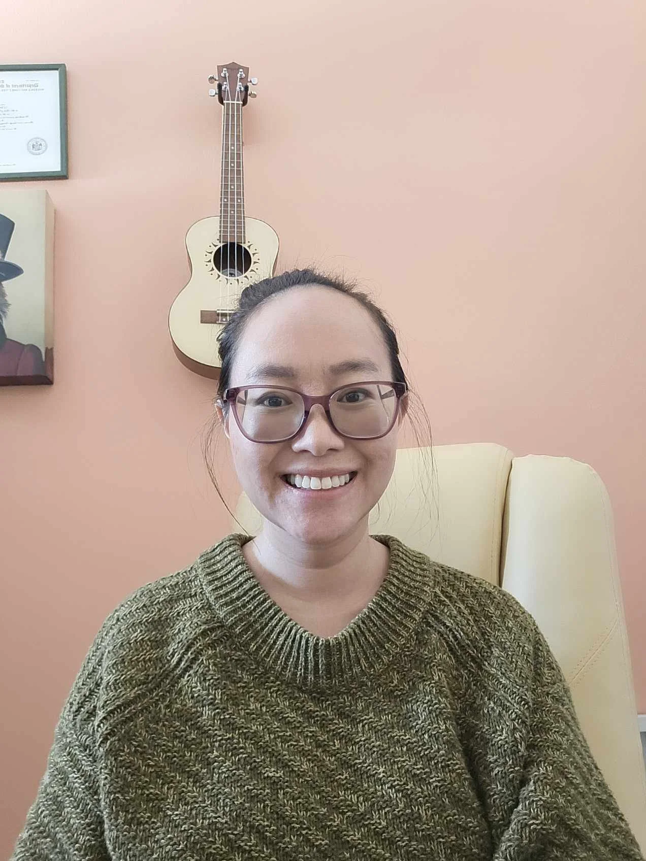 A woman wearing a green sweater, with glasses. Coral color background.