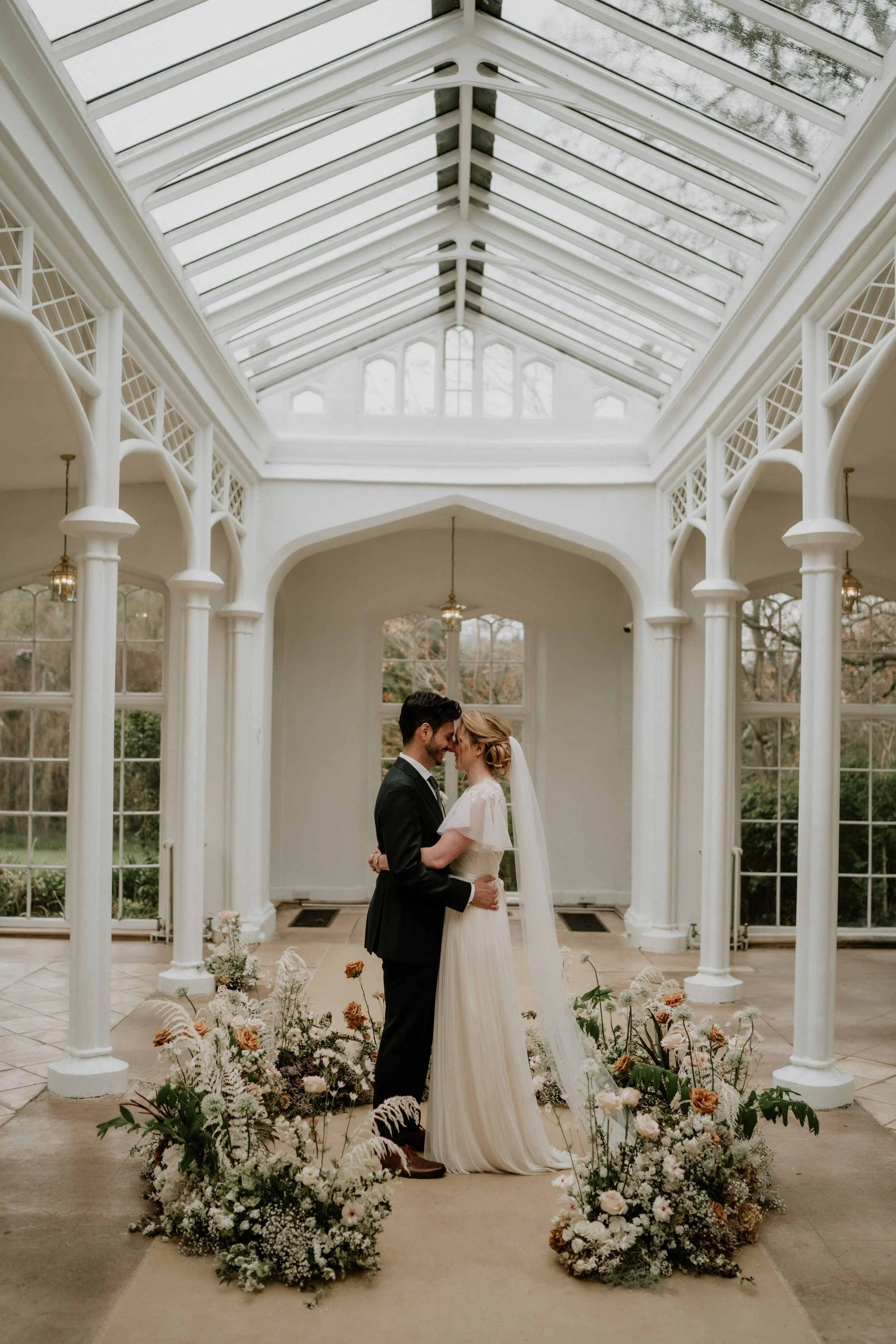 bride and groom hugging and kissing in a conservatory surrounded by flowers