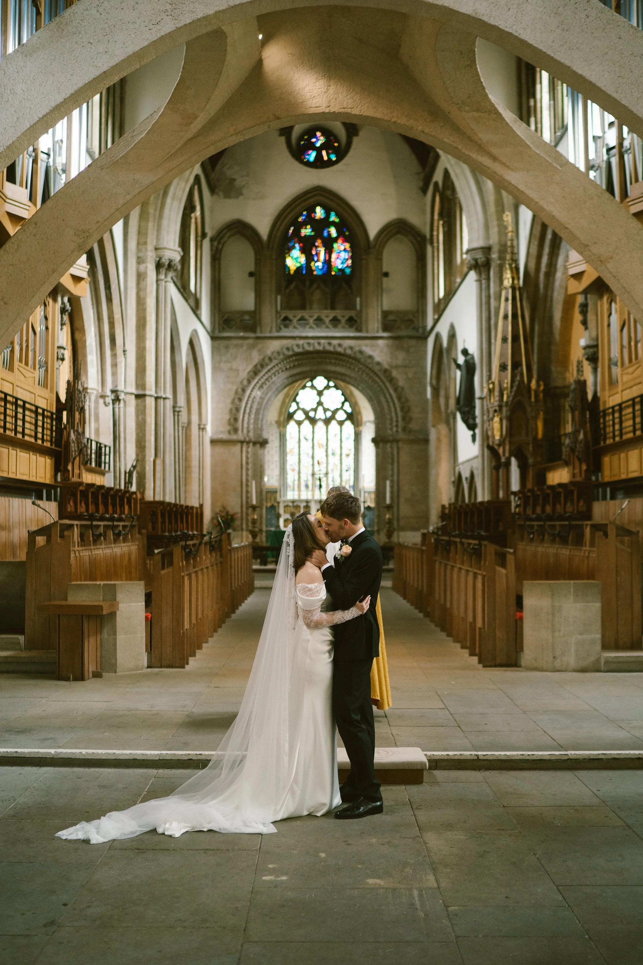 A bride and groom sharing a kiss inside a church with stained glass windows and wooden pews.