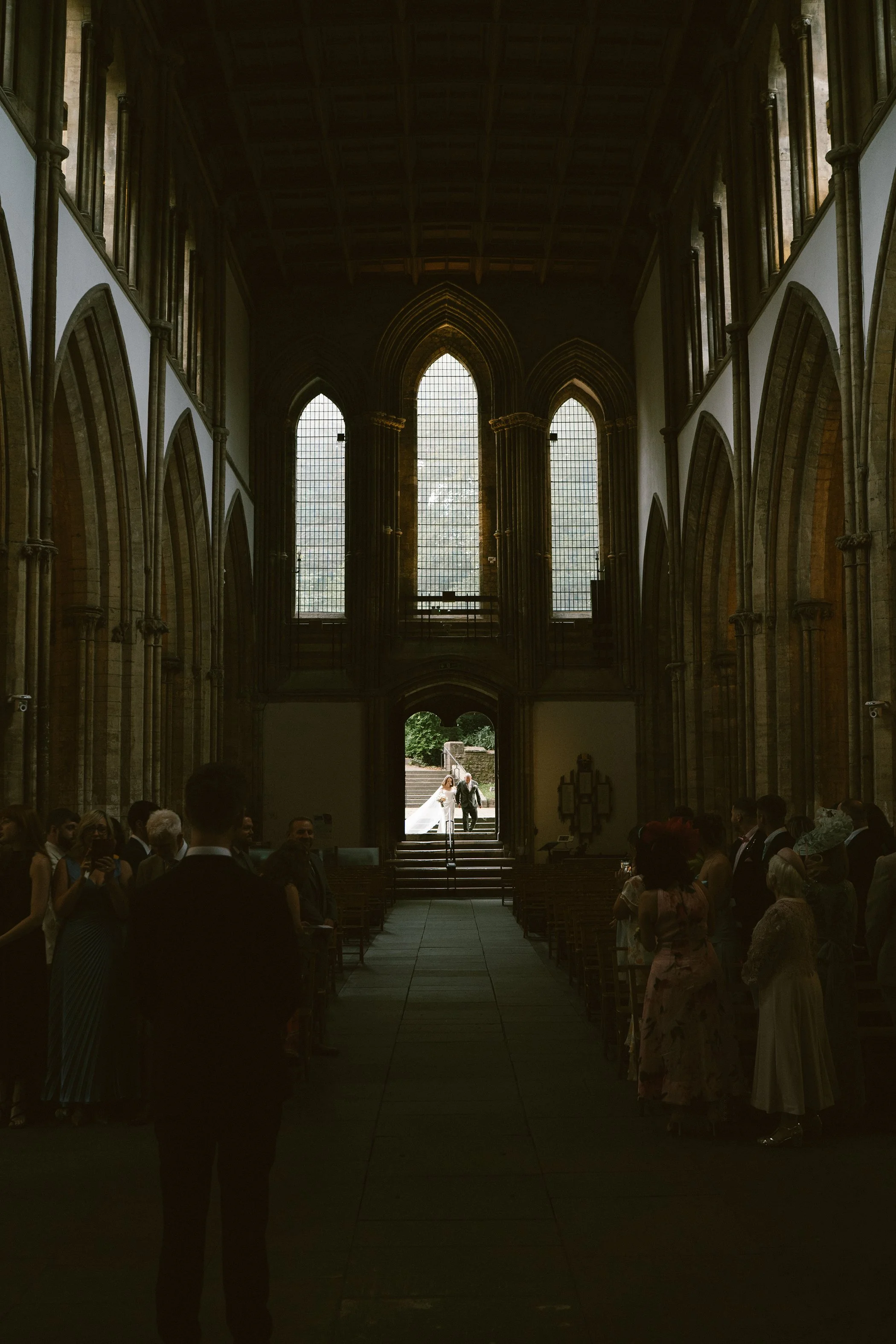 Interior of a church with tall stained glass windows, high vaulted ceiling, and people gathered for a wedding ceremony.