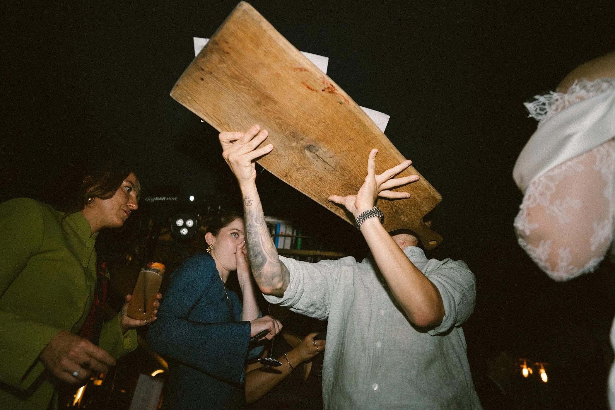 People at a bar holding a large wooden cutting board upright.