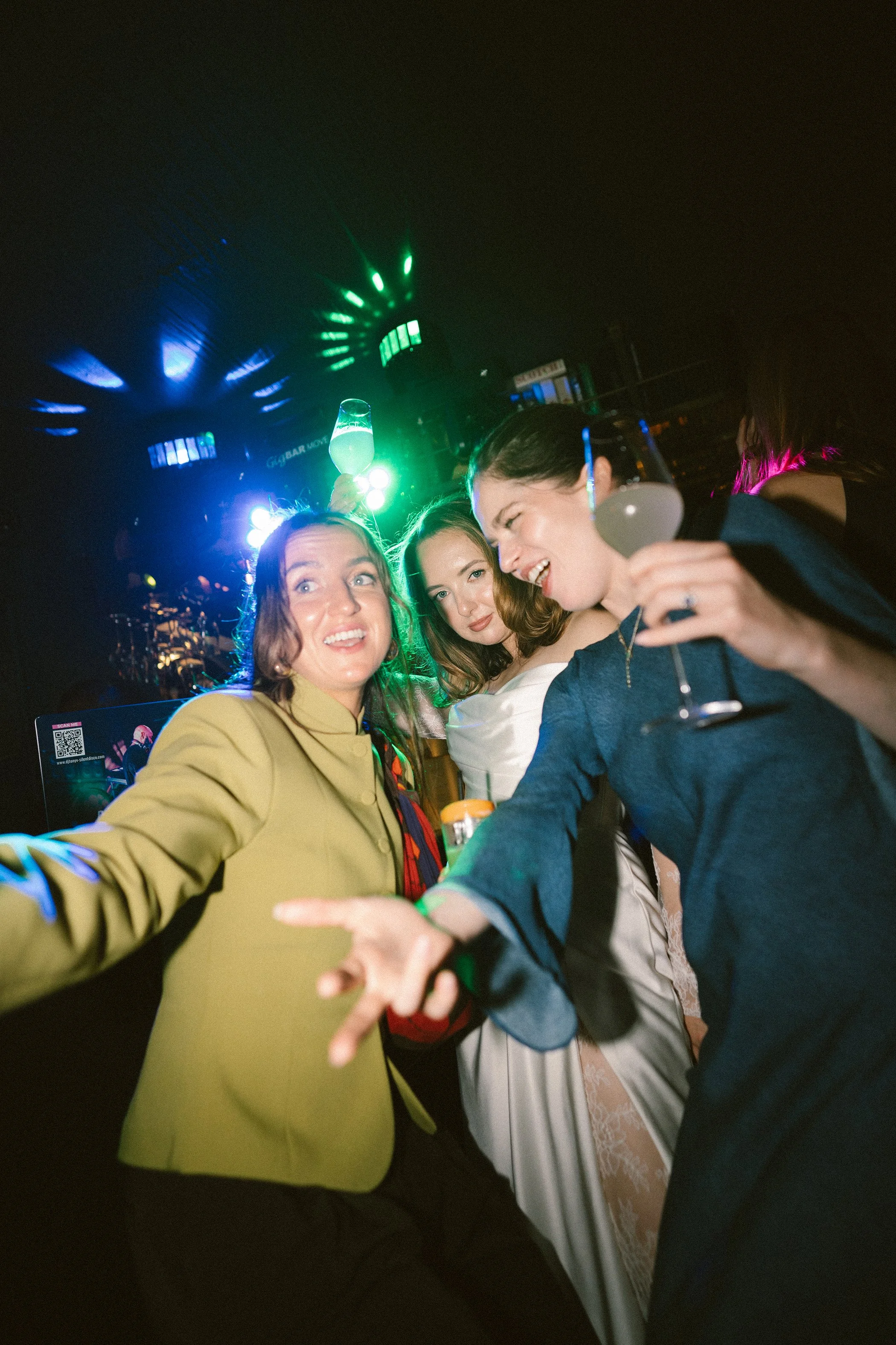 Three women in a nightclub, taking a selfie while holding glasses of champagne. They appear to be enjoying the night, with colorful lights and a lively atmosphere.