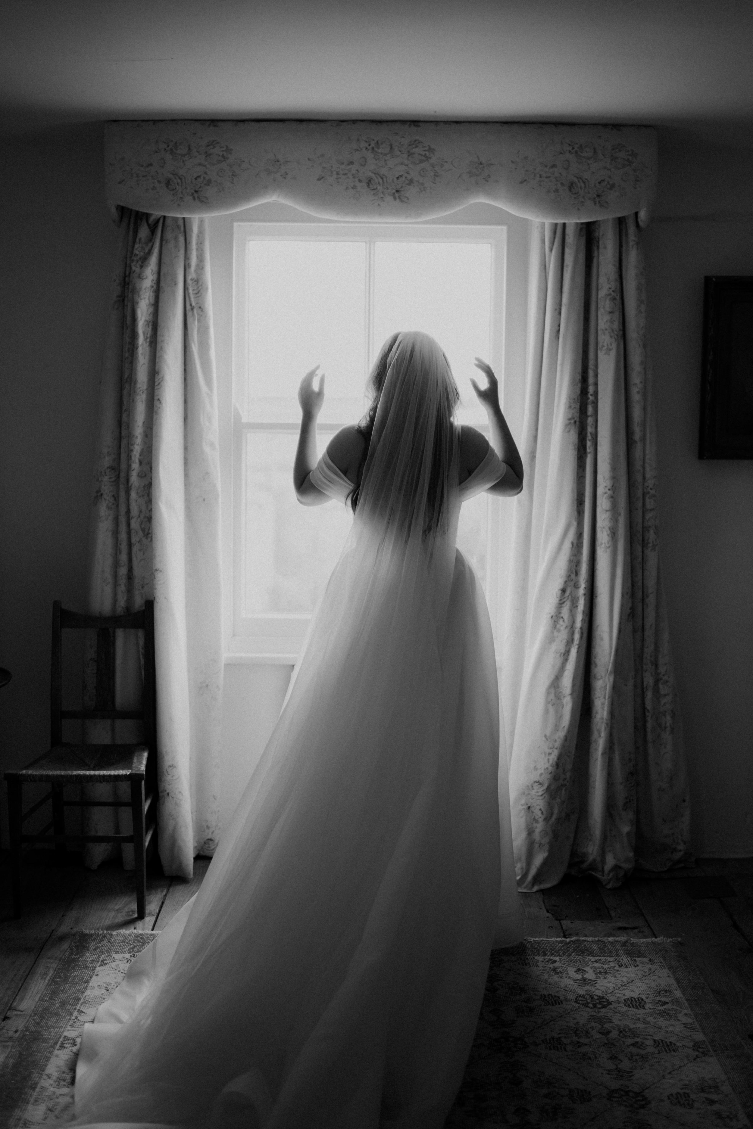 Bride putting her wedding dress on by a window