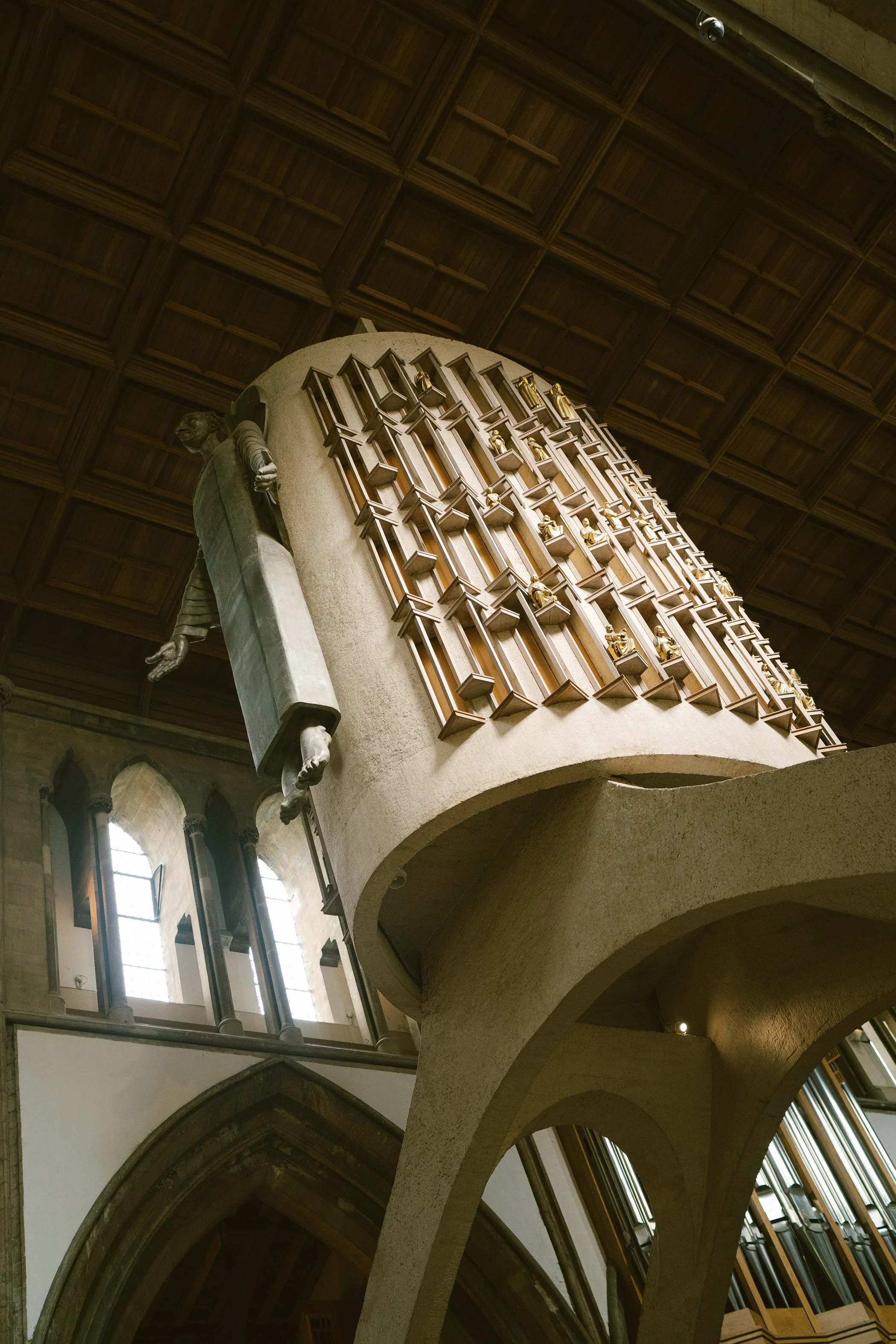 Inside view of a historic building with arched ceilings, large windows, and a prominent wooden staircase with decorative woodwork and statues.