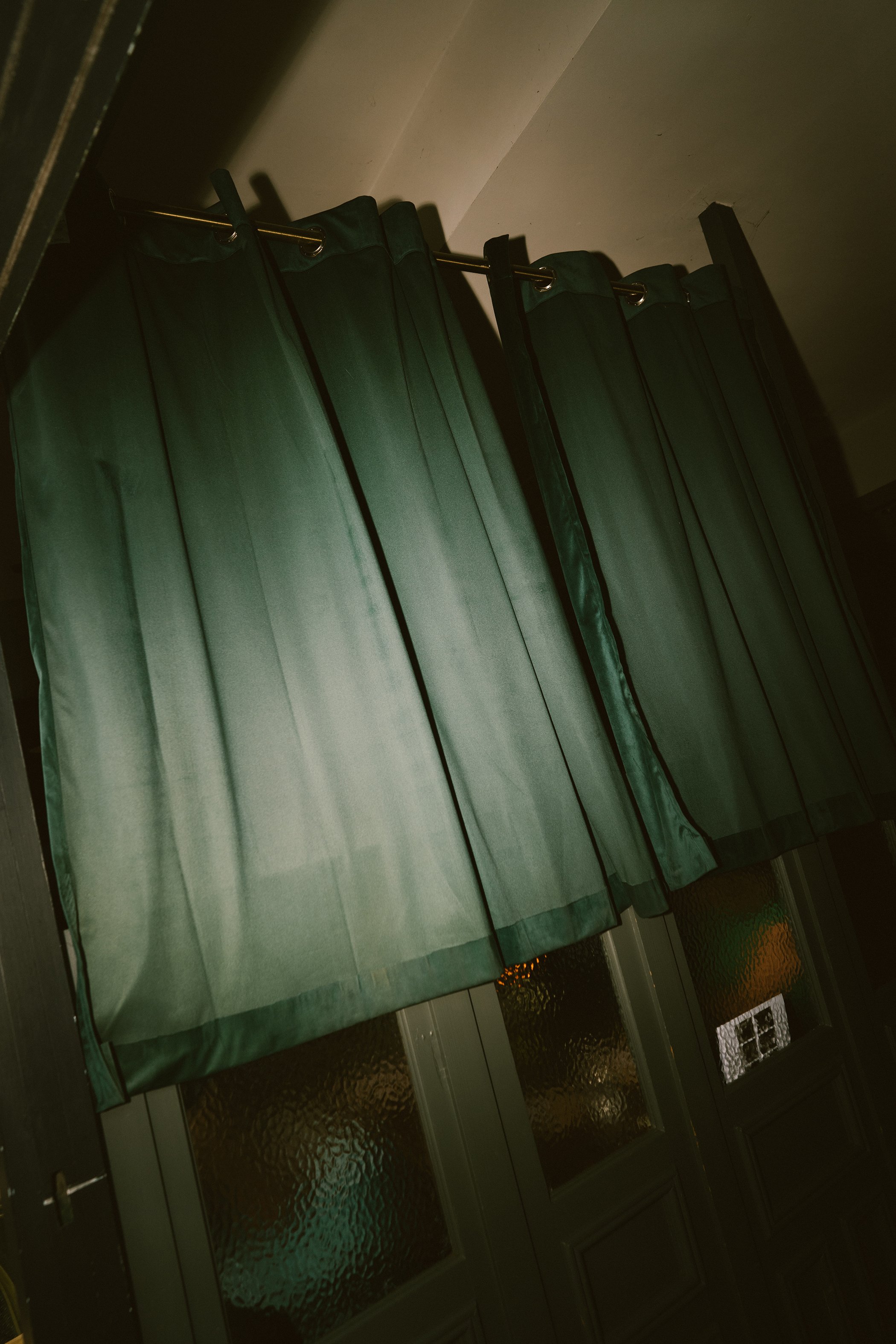 Green curtains hanging in front of a glass door with textured glass panels, part of a house or building entryway.
