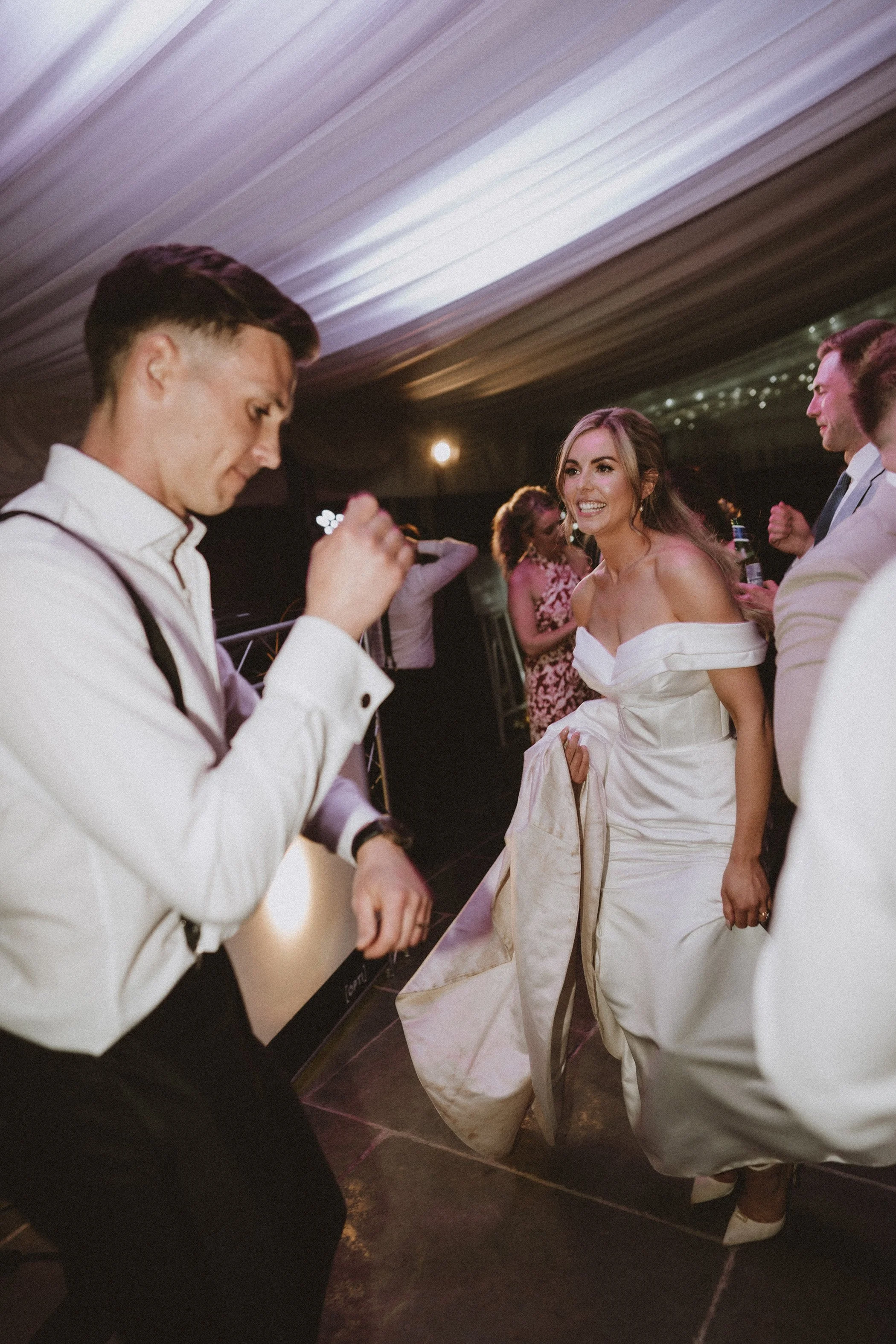 Bride and guests dancing at wedding reception with warm lighting and festive atmosphere.