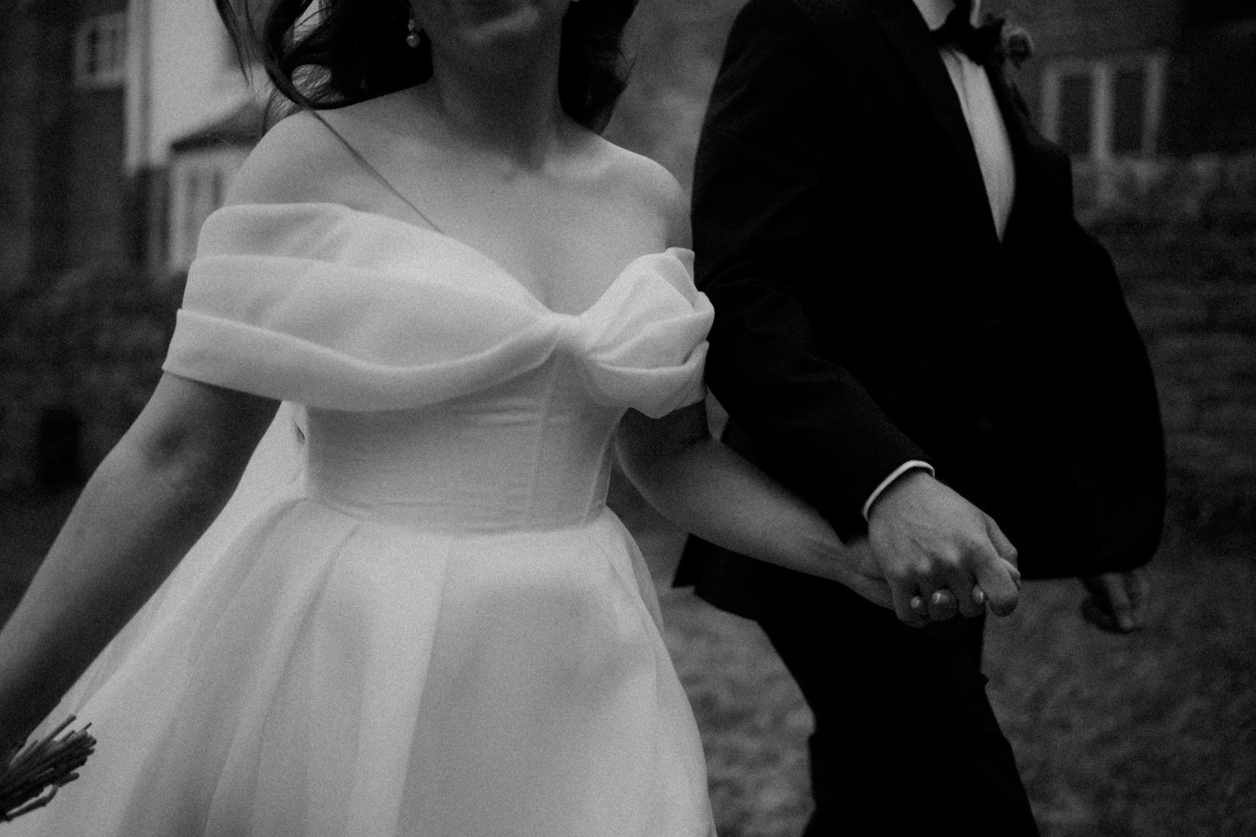 A black and white photo of a bride and groom holding hands during their wedding, with only the upper bodies visible.
