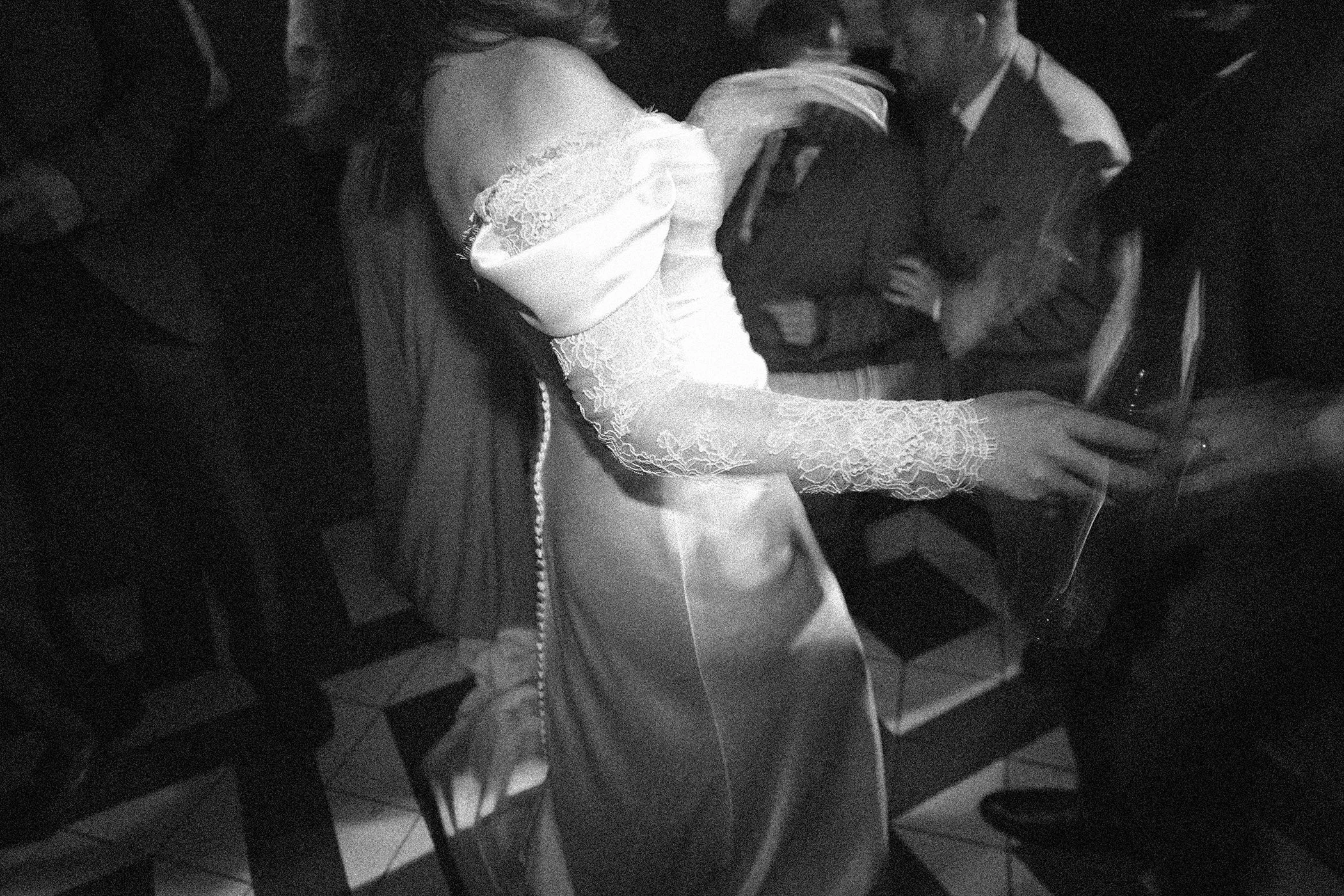 A black and white photo of two people, a woman wearing a lace dress and a man in a suit, sitting closely together with their heads near each other, possibly sharing a kiss or whispering.