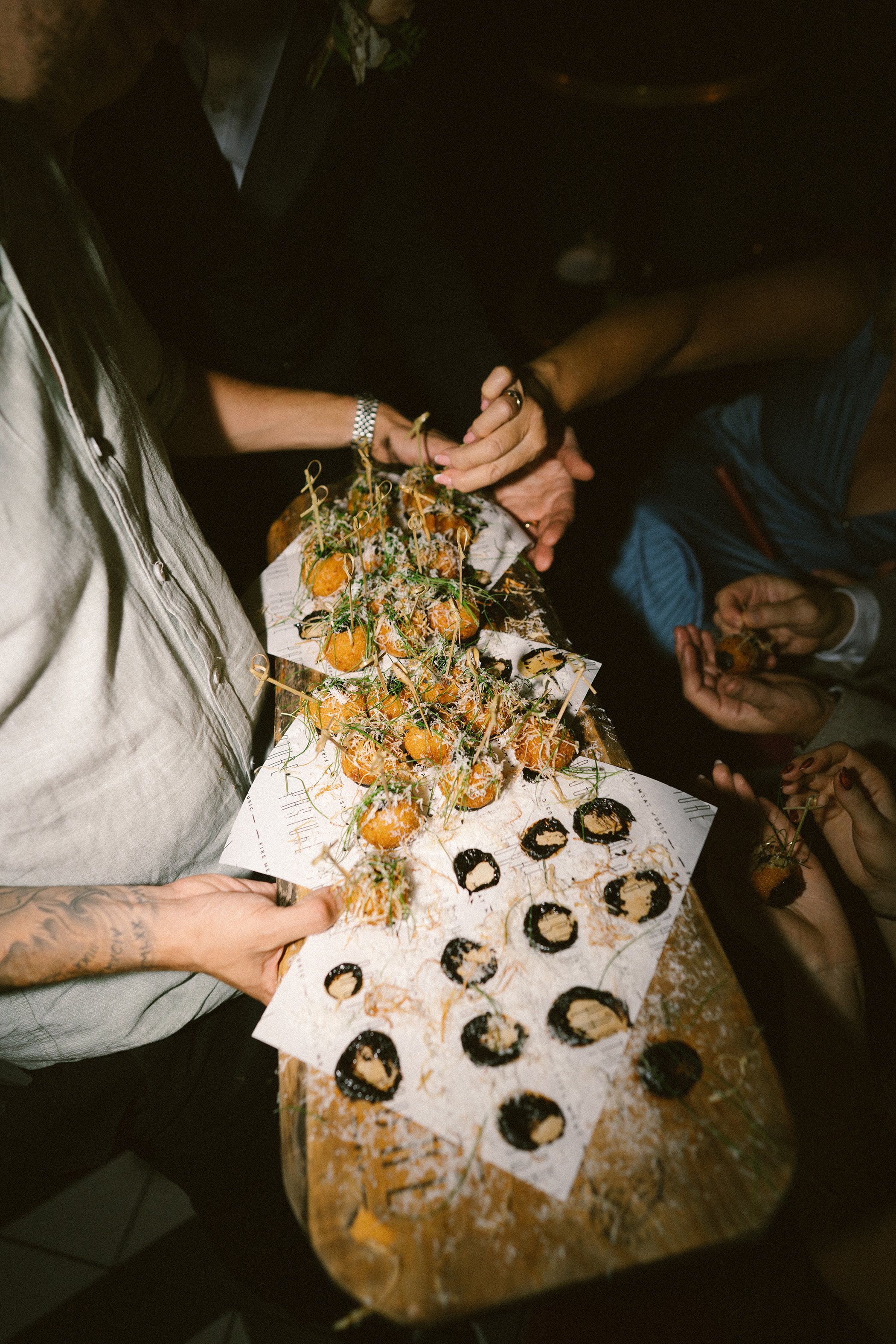 People at a party holding a tray of decorated desserts, including small cakes with toppings, on a wooden table.
