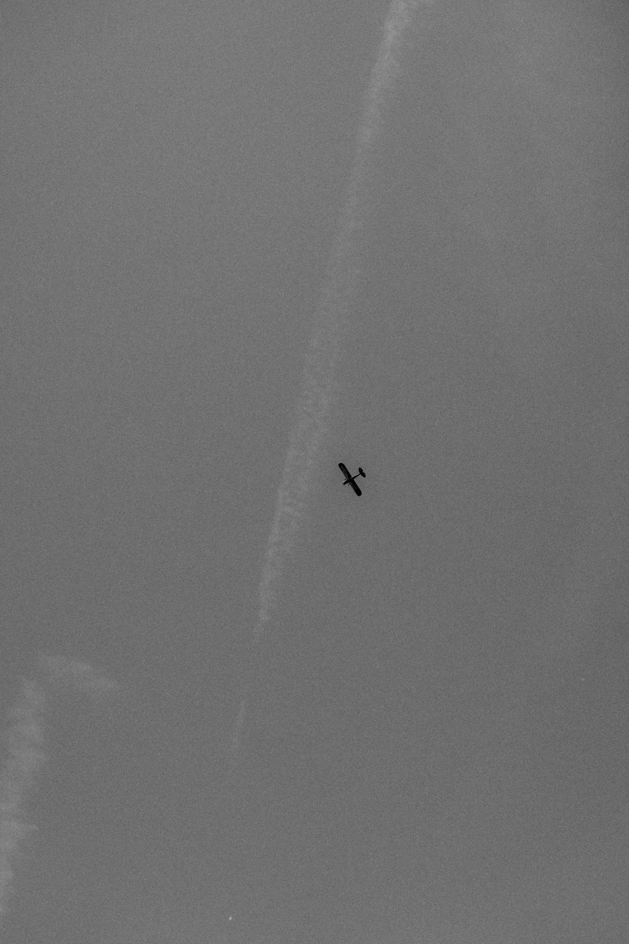 A small airplane flying through the sky, leaving a contrail behind.