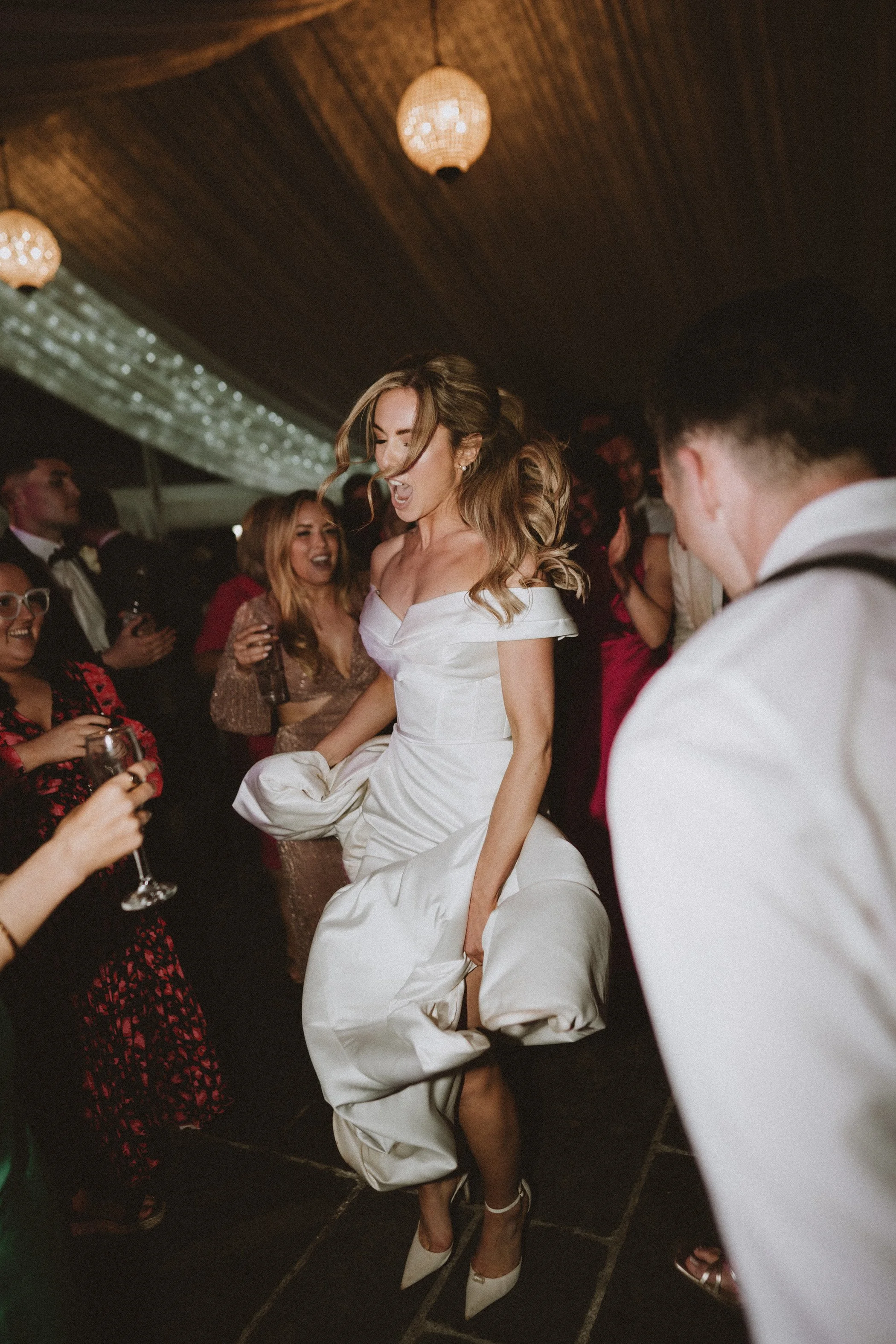 A woman in a white dress dancing and laughing at a party surrounded by other guests.