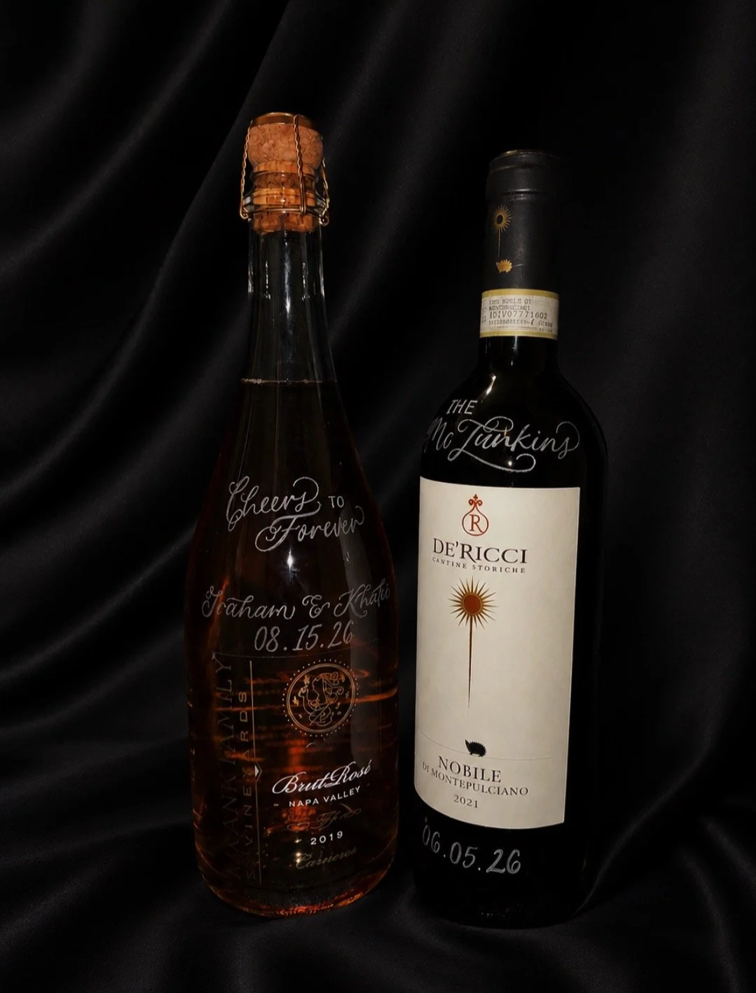 Two bottles of wine against a black background, one with a cork and a handwritten message and the other with a black and white label and a handwritten date.