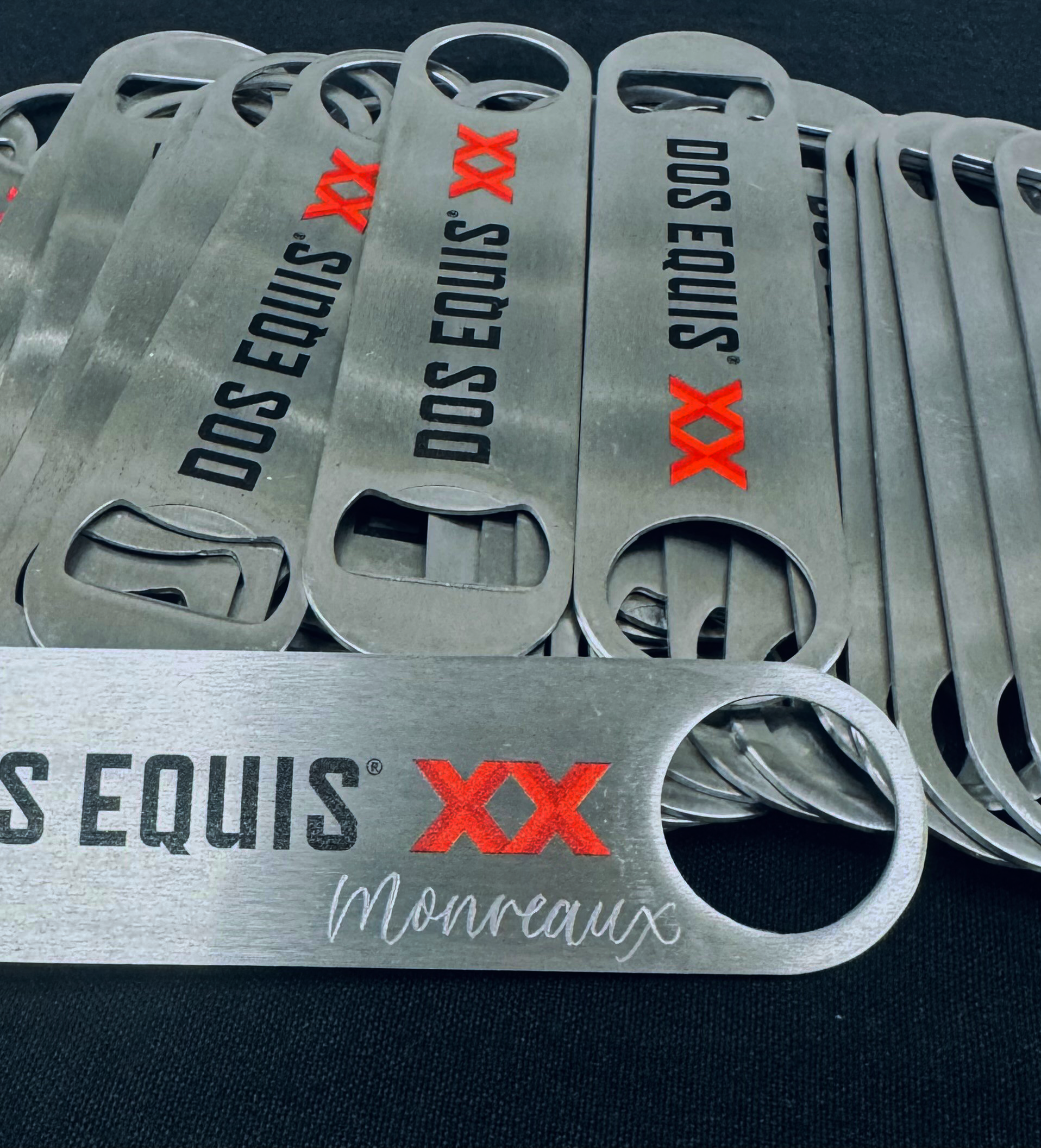 Multiple metallic bottle openers with the text "DOS EQUIS XX" and "Montraux" printed on them, stacked together.