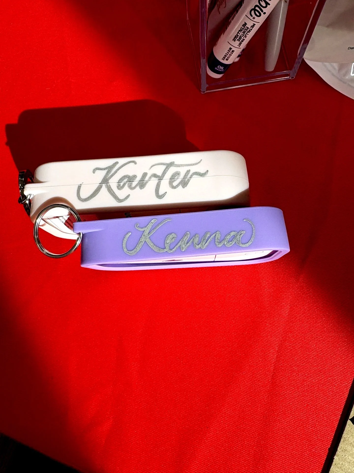 Two LED light-up wristlets with names 'Katar' in white and 'Kanna' in purple on a red surface.