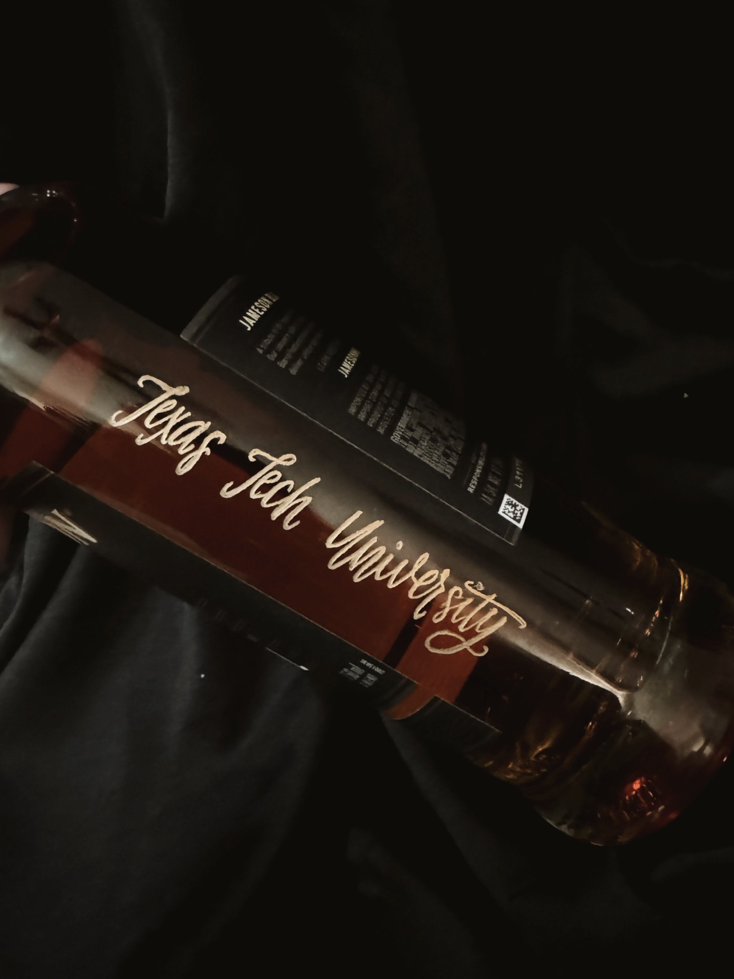 Close-up of a Jack Daniel's whiskey bottle resting on a dark surface, with part of a drinking glass visible in the background.