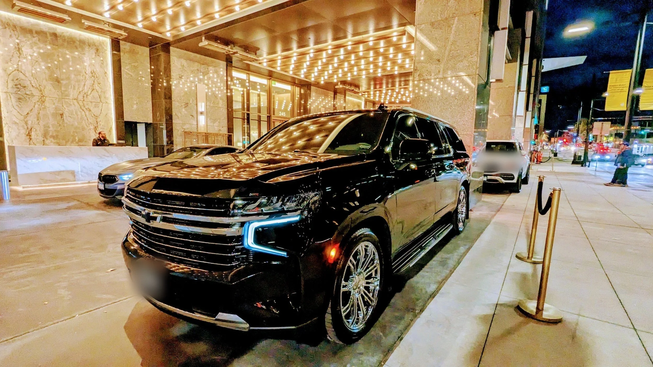 For Sure Luxury 2025 Limo Custom Suburban waiting at a downtown Minneapolis hotel entrance at night for a point-to-point transfer
