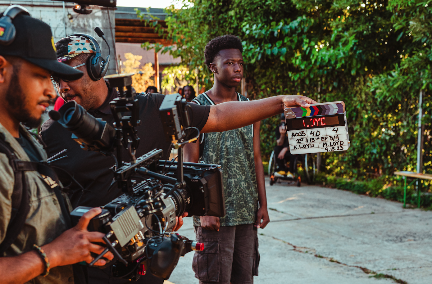 Film crew on set holding a clapperboard and operating a camera outdoors.