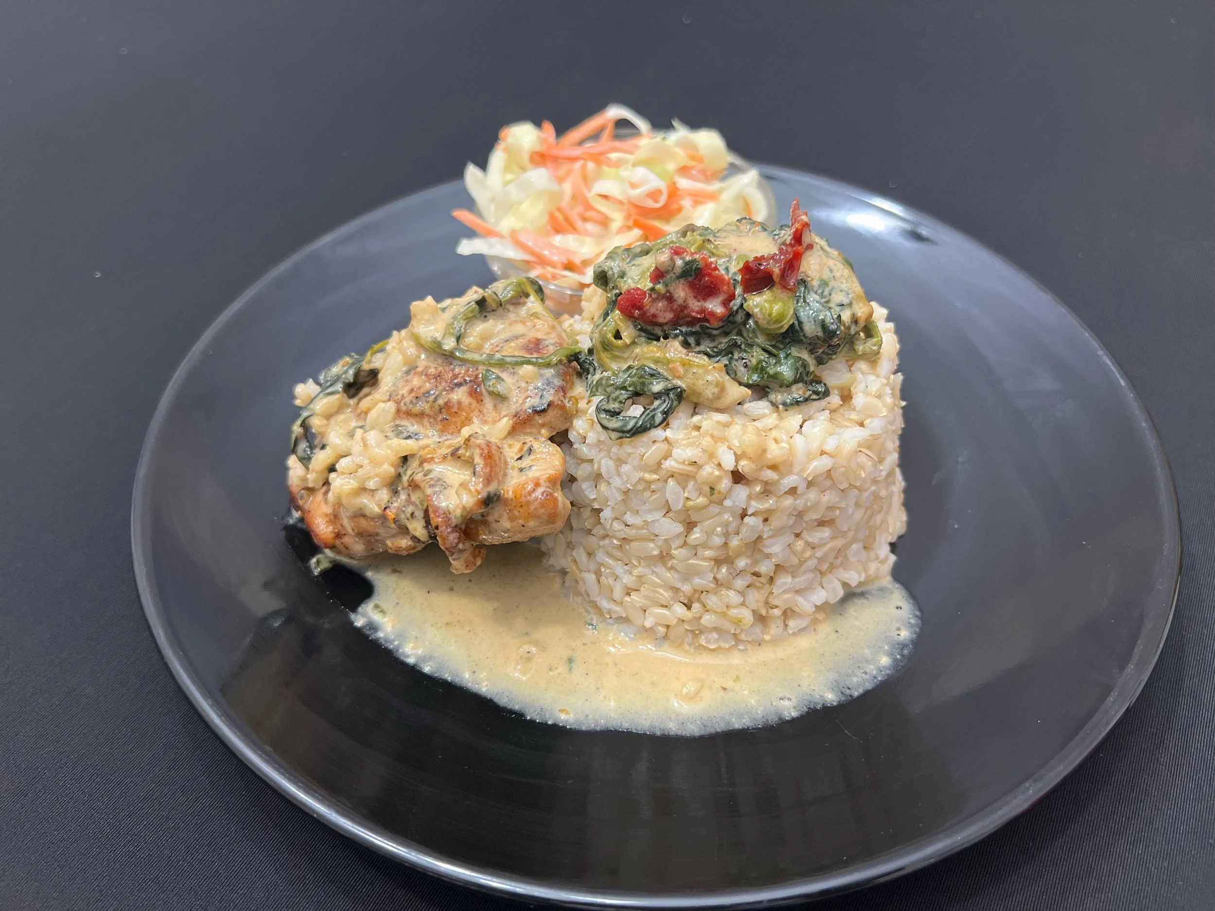 Creamy stew with chicken, vegetables, and rice served on a black plate with a side of coleslaw.
