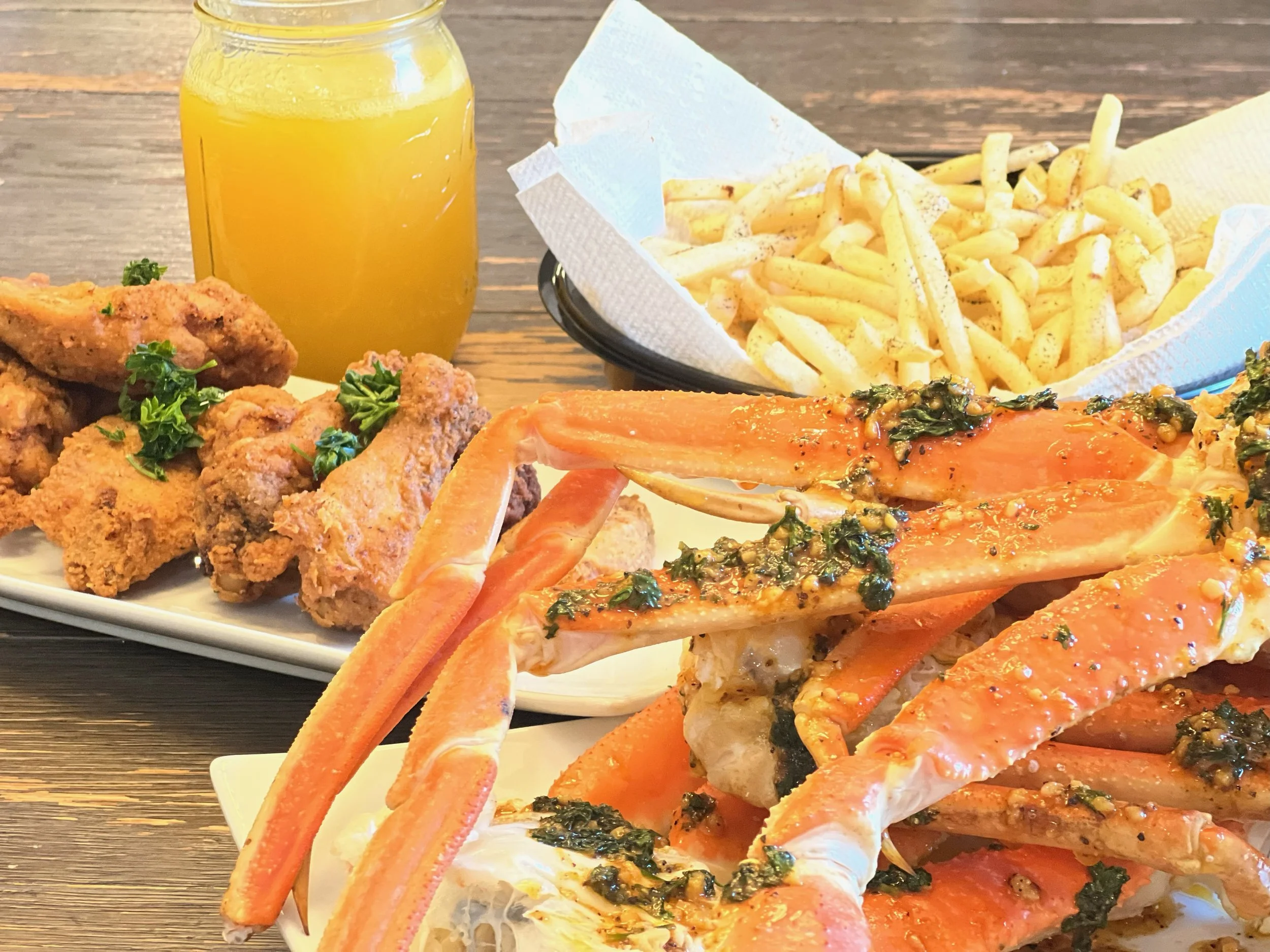 Crab legs with garlic and herbs, fried chicken pieces garnished with parsley, a side of French fries, and a glass of orange juice.