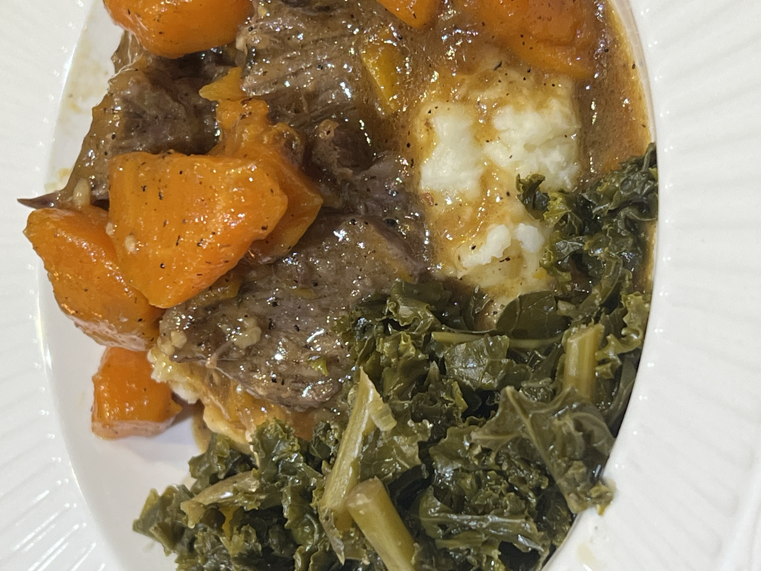 Hearty beef stew with carrots, potatoes, dark leafy greens, and herbs served on a white plate.