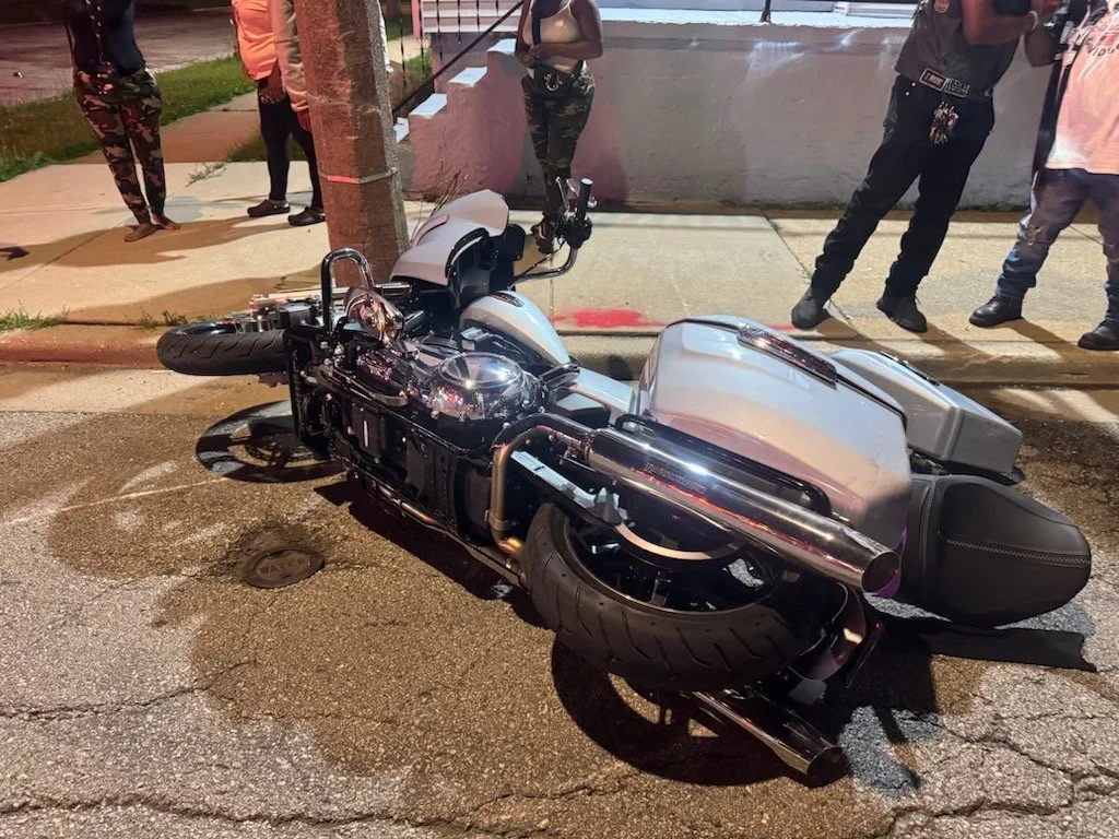 A cruiser-style motorcycle lying on its side on the street, with people standing nearby, during nighttime.
