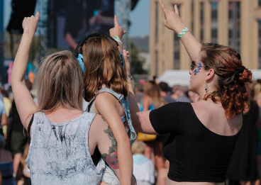 A group of women and girls at an outdoor event, some raising their hands, with buildings in the background.