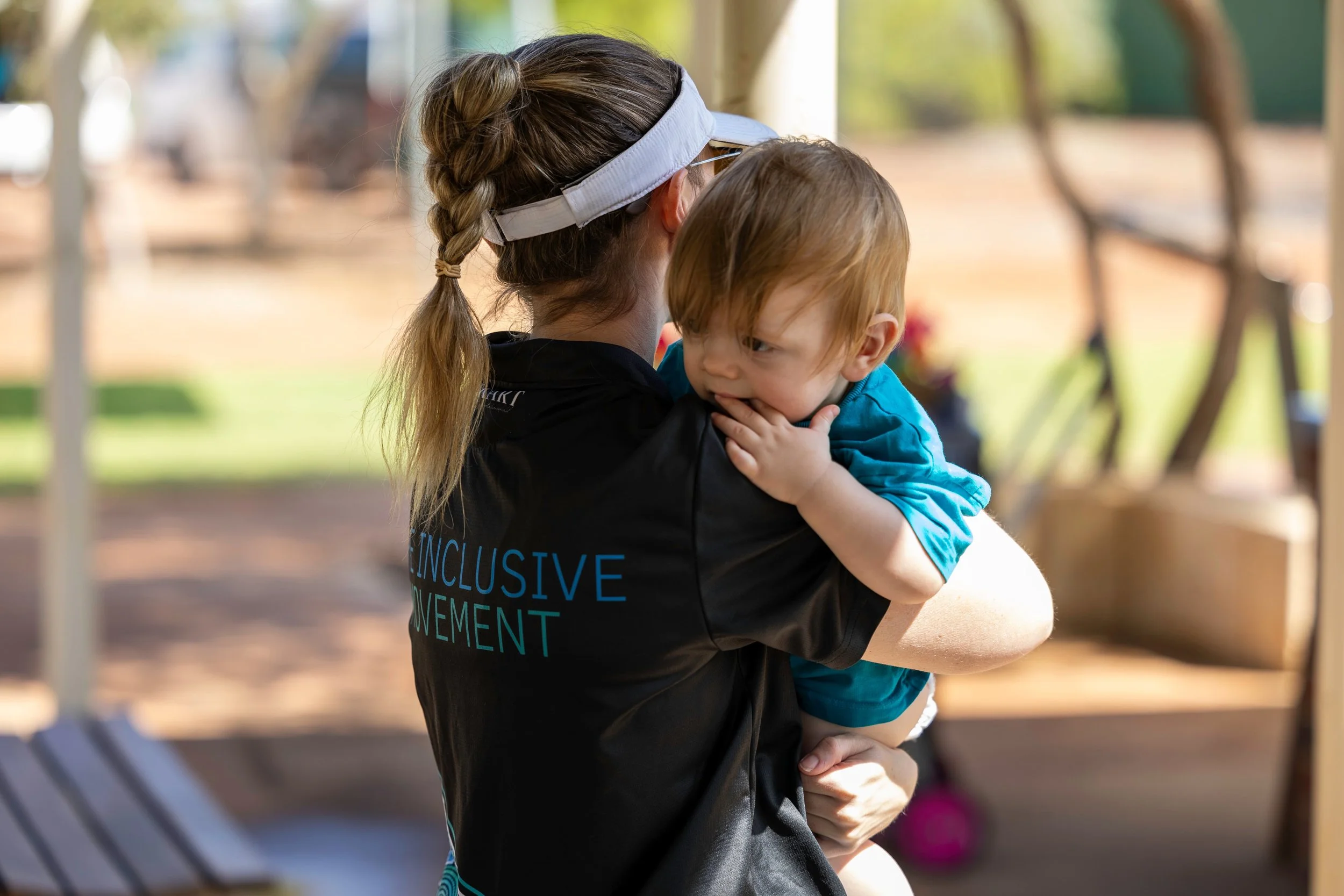 A woman with a braid and wearing a black shirt holding a young child in an outdoor setting.