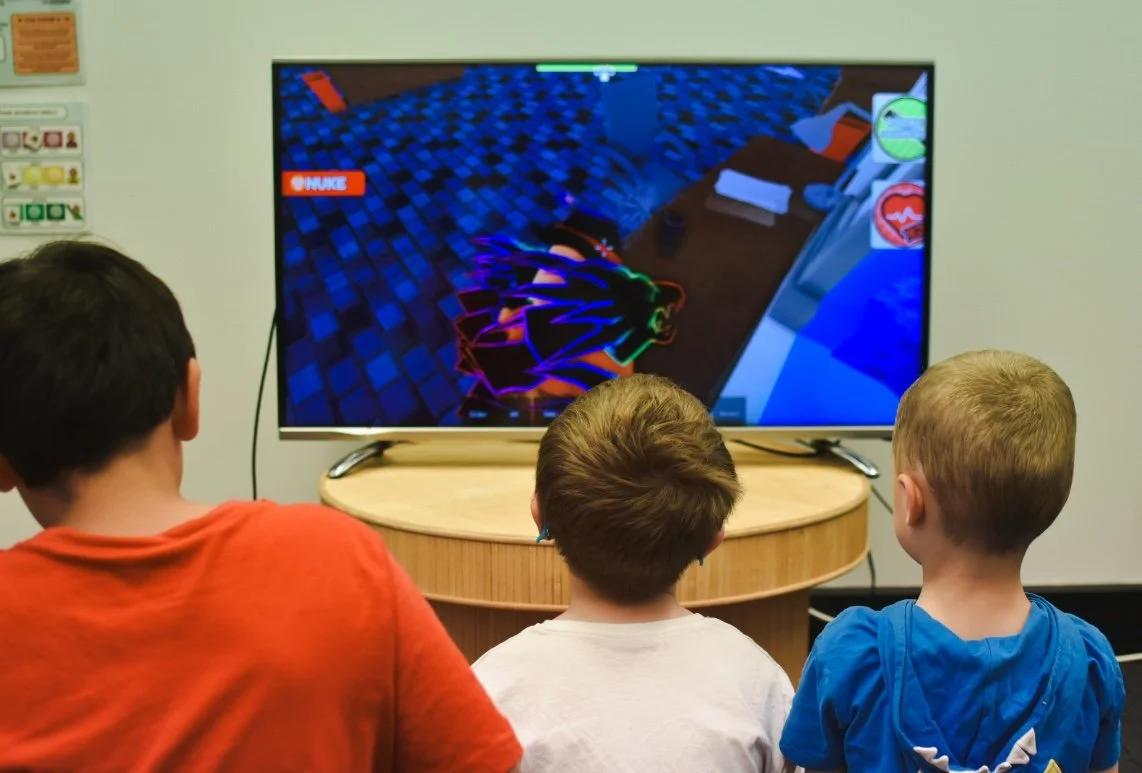 Three children watching a video game on a TV screen in a room with light-colored walls.