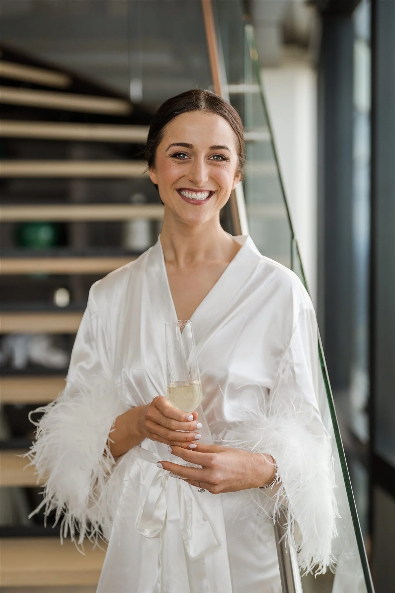 Bride with fresh face of makeup smiling at the camera and holding a glass of champagne