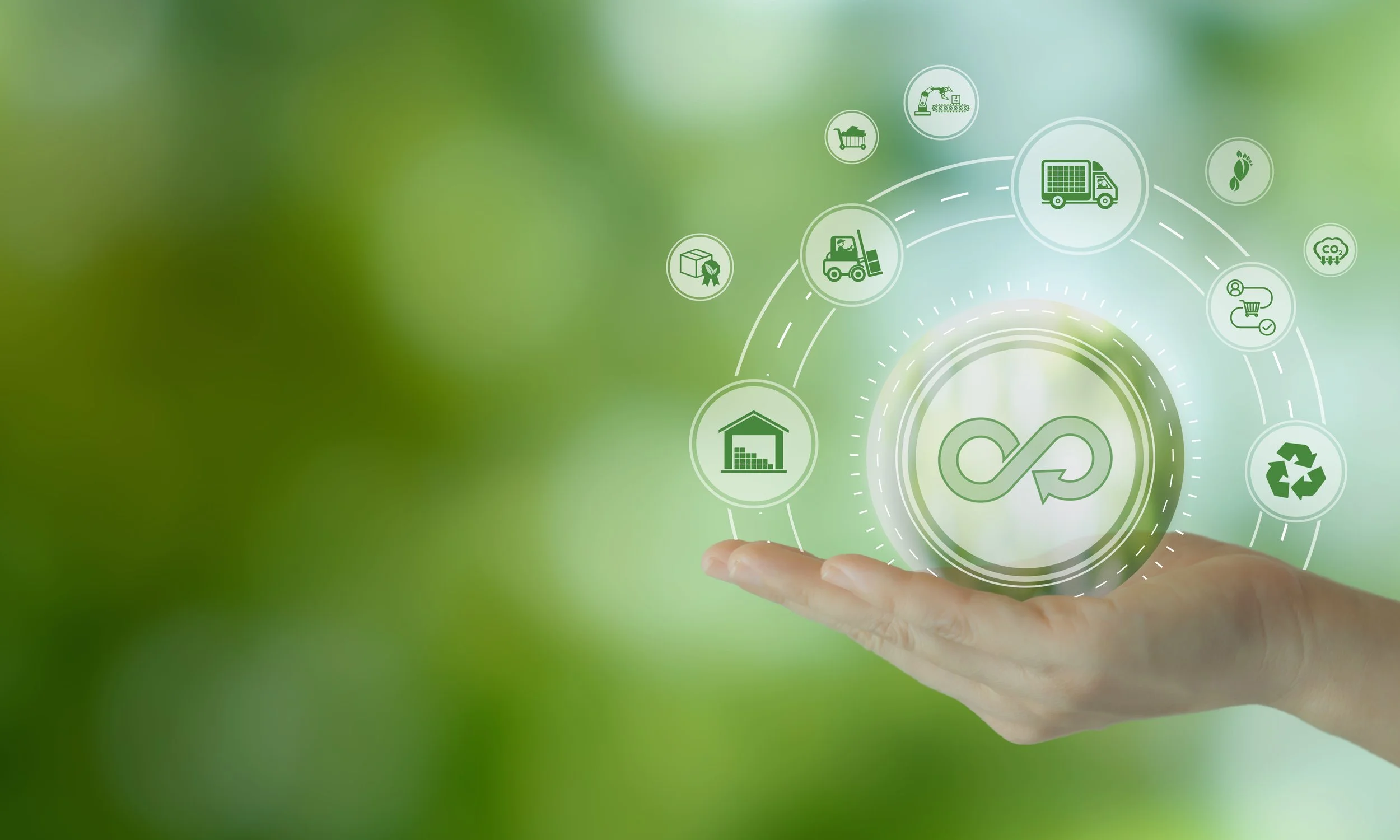 A hand holding a transparent digital infographic with icons representing recycling, logistics, manufacturing, agriculture, and sustainability, set against a blurred green background.