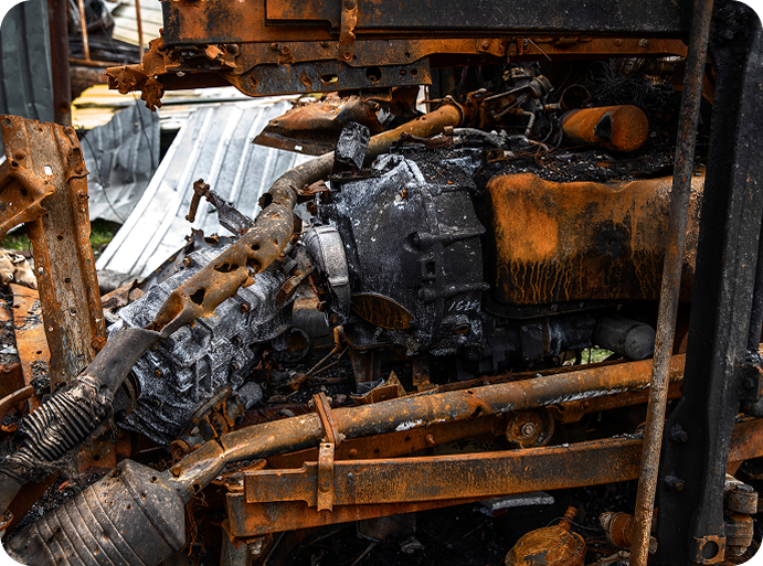 Close-up of a rusted and damaged vehicle engine with blackened, corroded metal parts.
