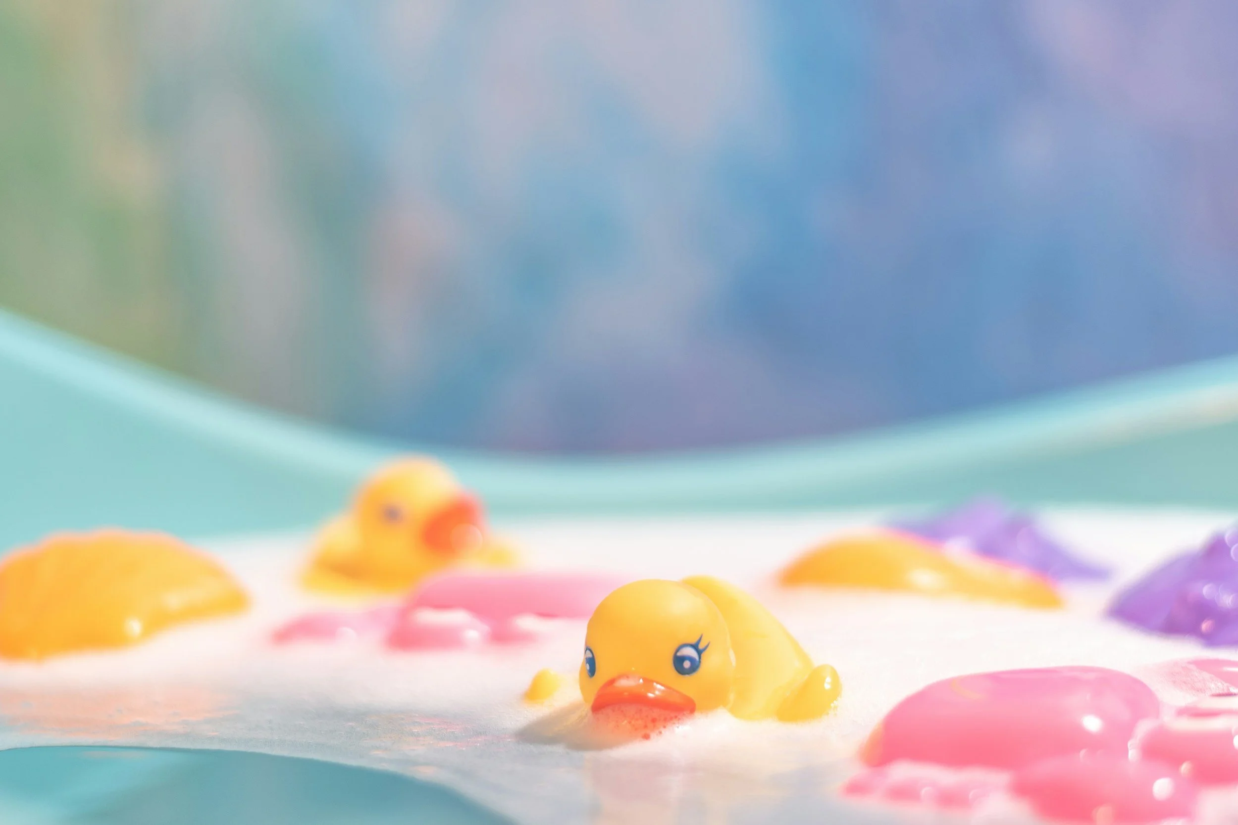 Colorful rubber duck toys floating in a pink, purple, and white foam bath.