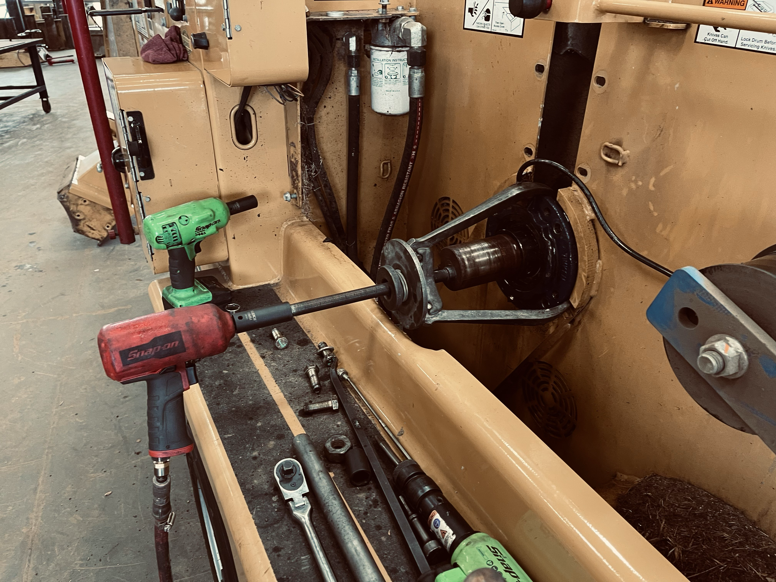 Close-up of machinery being repaired with power tools, wrenches, and parts on a workbench in a workshop.