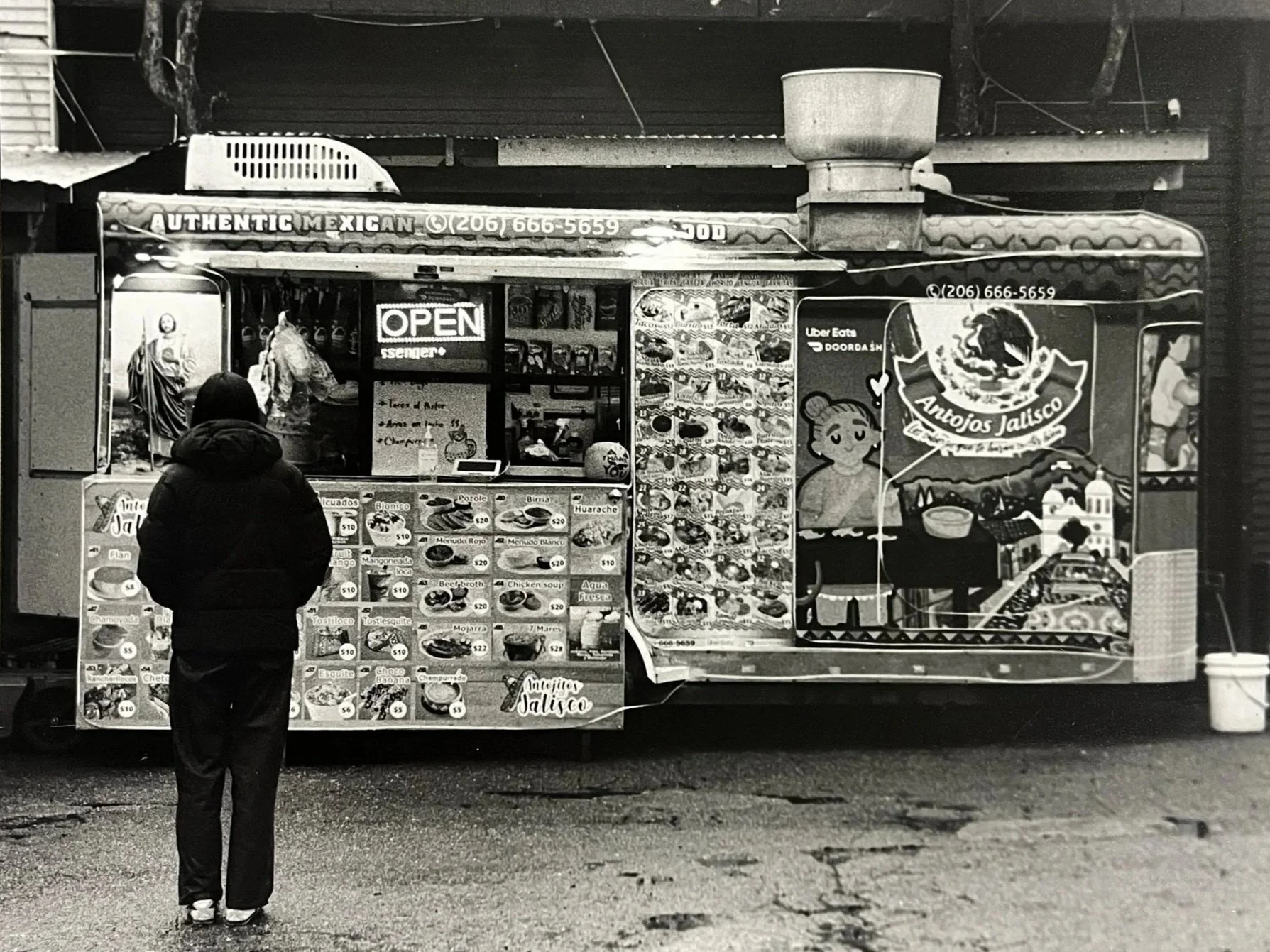 A person with a hoodie and pants standing in front of a Mexican food truck.