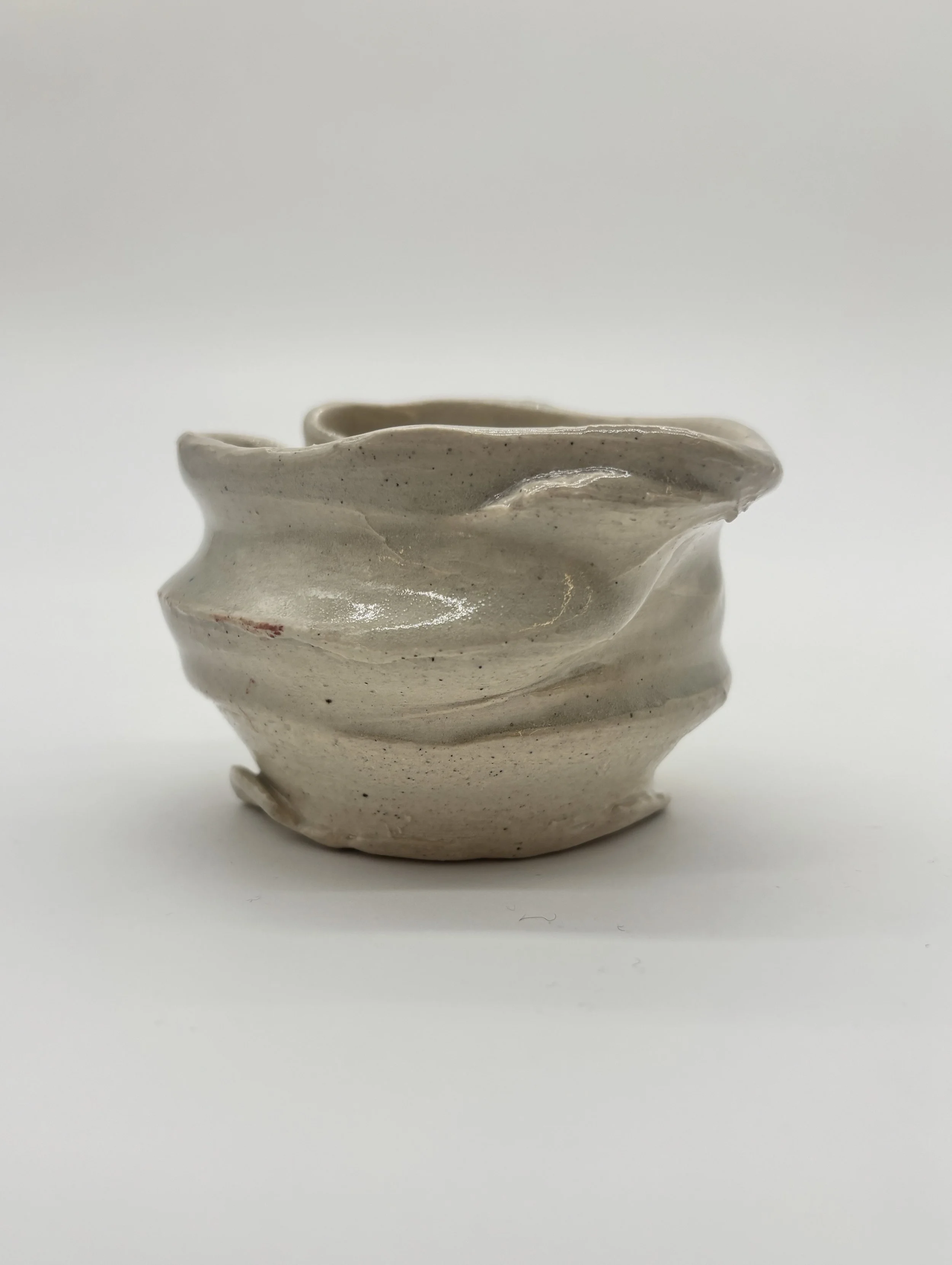 Cream-colored, irregularly shaped ceramic cup with a textured surface and a slightly wavy rim, set against a plain white background.