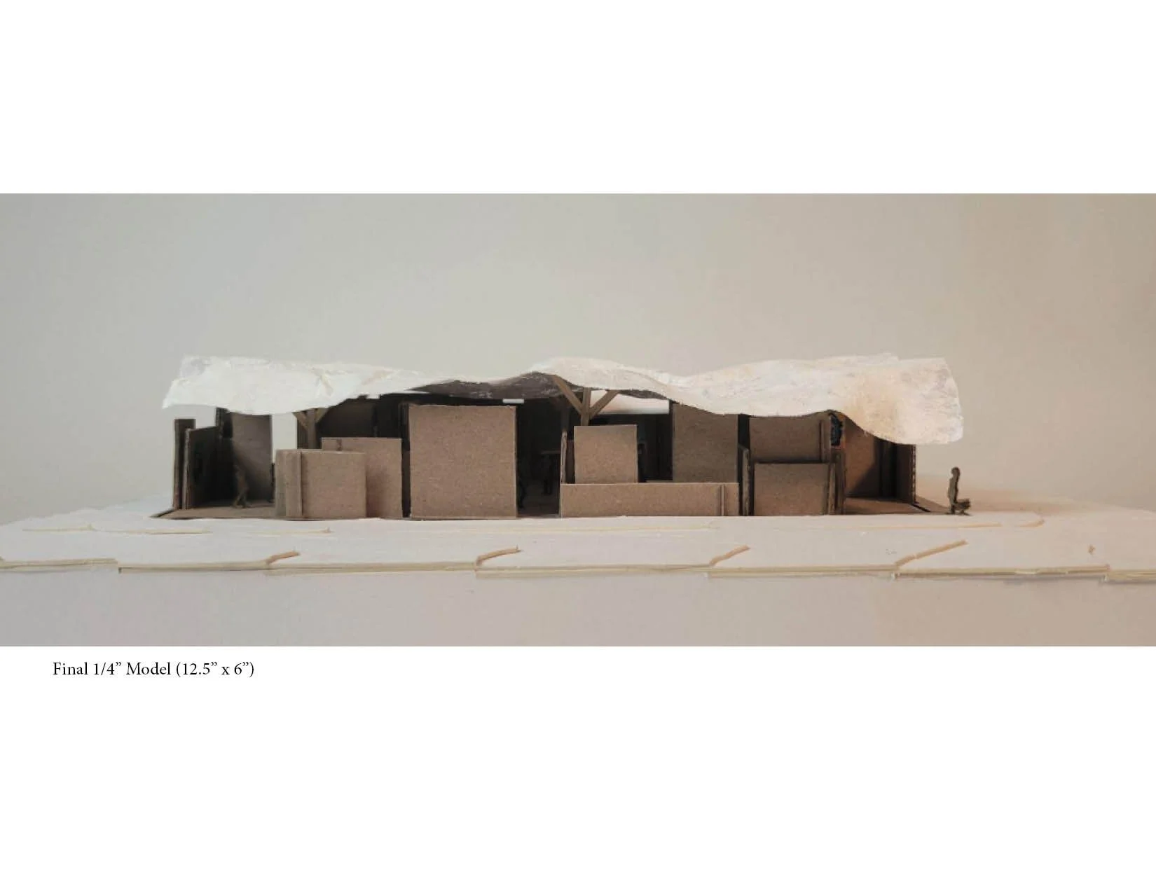 Architectural model made of cardboard and paper, representing a building or structure with a wavy roof, placed on a white surface.