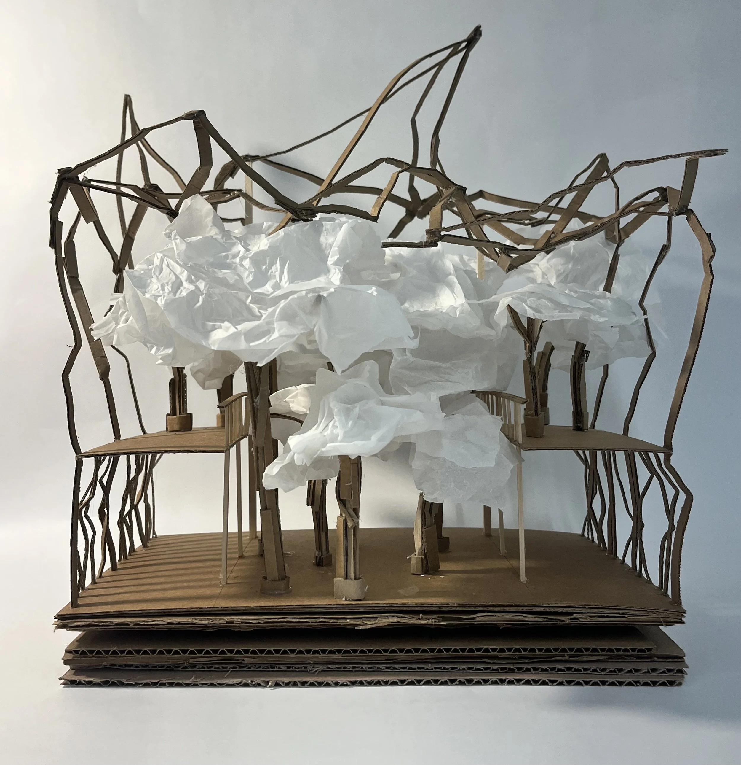 A detailed architectural model made of cardboard and paper, featuring a unique structure with multiple platforms, interconnected by thin, branching supports. There are crumpled white paper elements resembling clouds or foliage, adding artistic detail