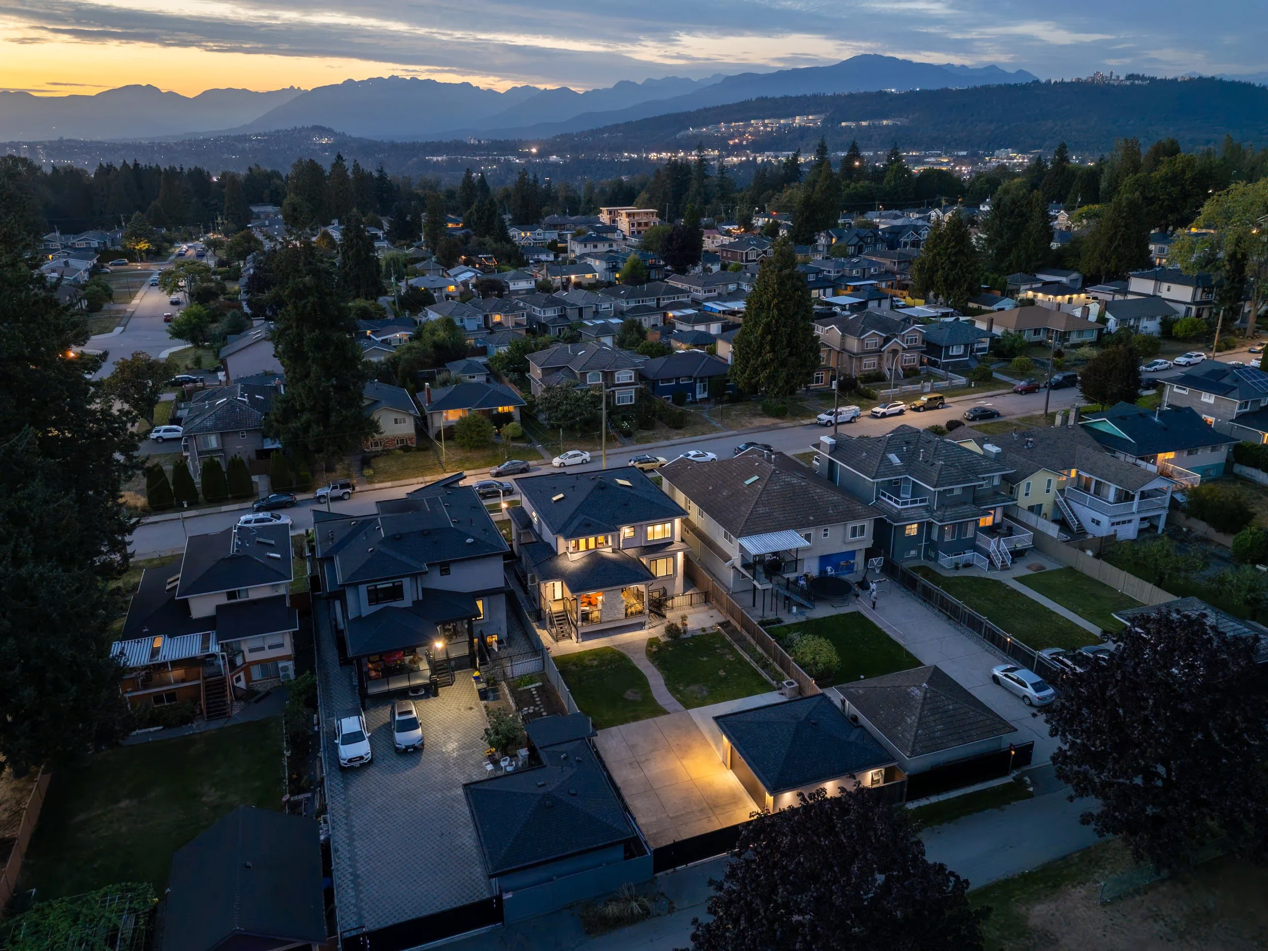 A tall modern glass building with a square orange opening on its side, set against a cityscape and mountainous horizon during sunset with clouds.