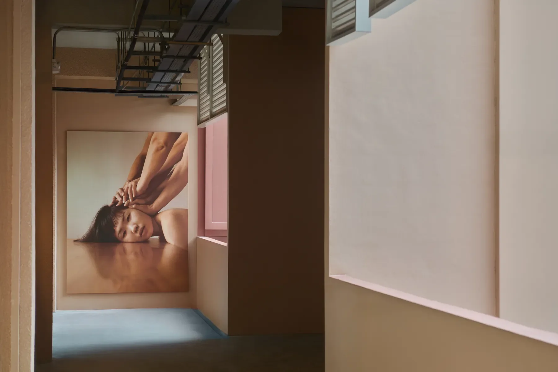 An art gallery wall featuring a large portrait of a woman with dark hair lying on her side with her hand touching her face, in muted colors.