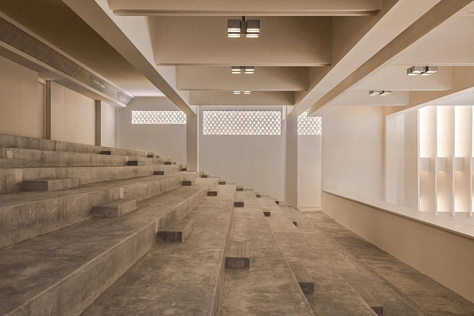 Modern interior with concrete stairs and white walls, ceiling lights, and ventilation system.