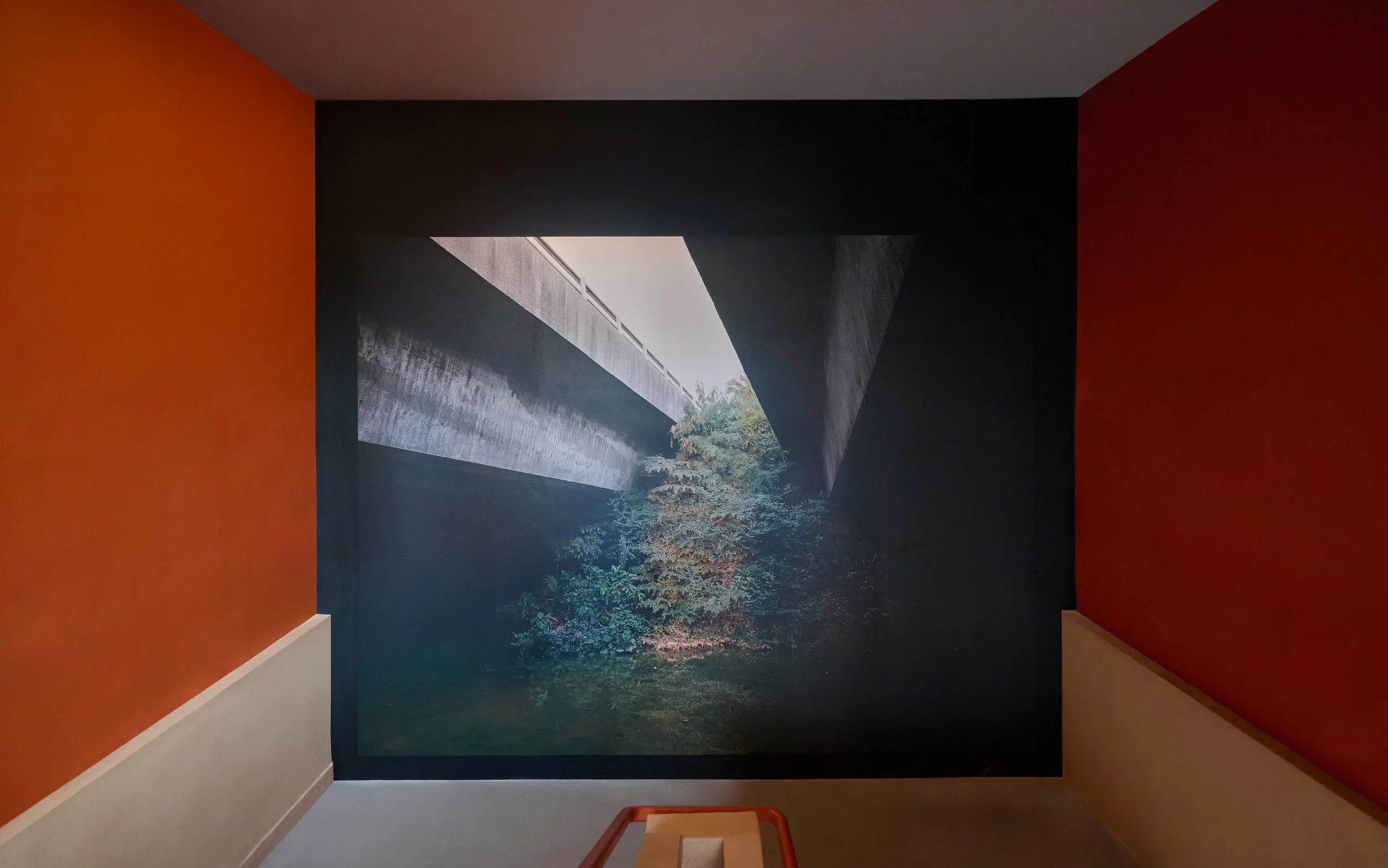 Interior room with orange and dark gray walls, featuring a large mural of a building facade and greenery on the back wall.
